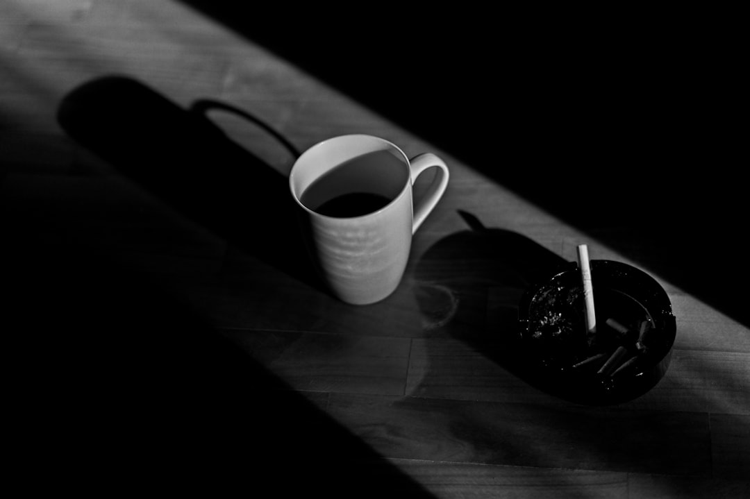 Taza de café y cigarro humeante en un cenicero sobre una mesa de madera. Metáfora de la clase trabajadora americana y las historias y libros de Raymond Carver