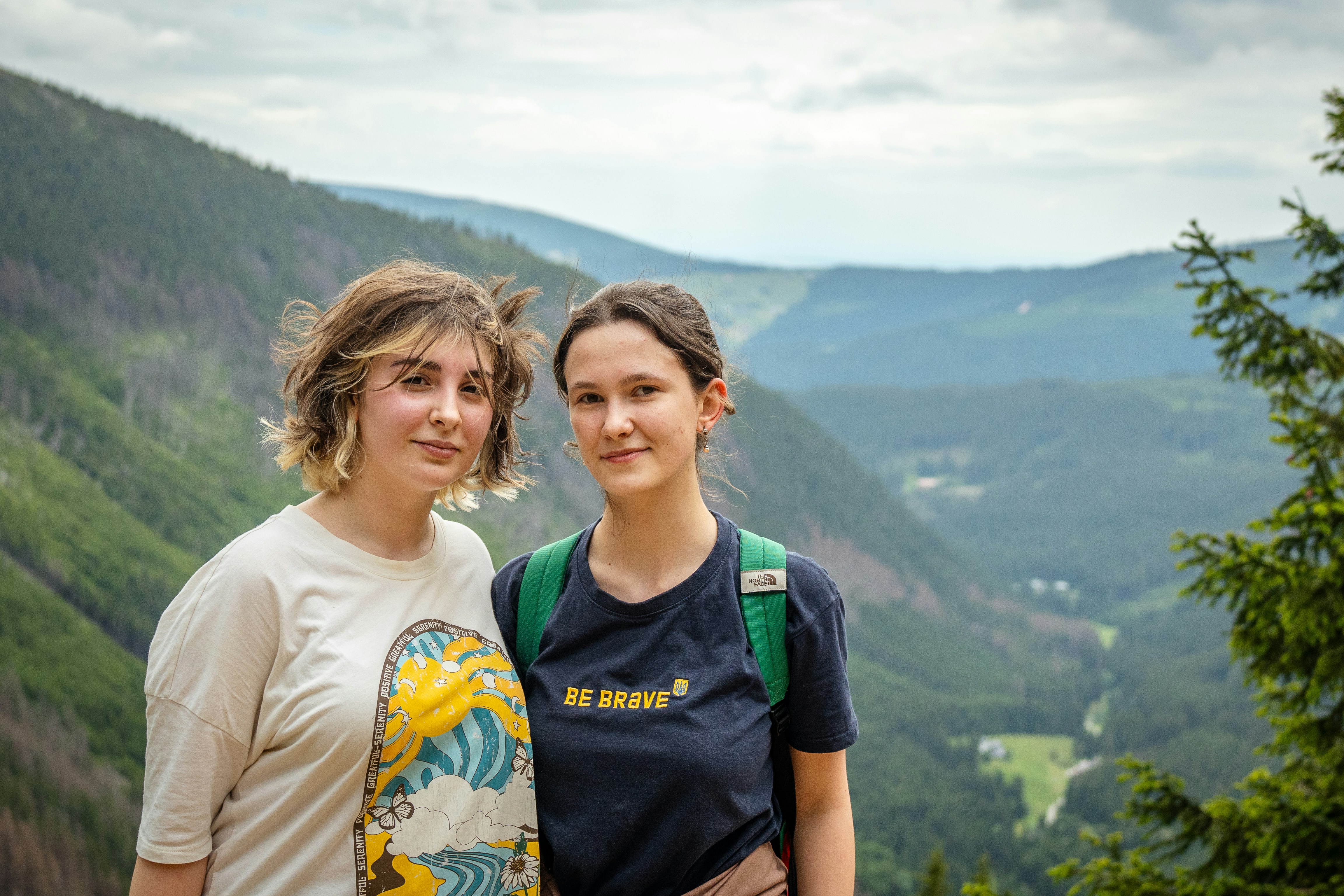 Two young women with a skateboard in a mountain landscape.
