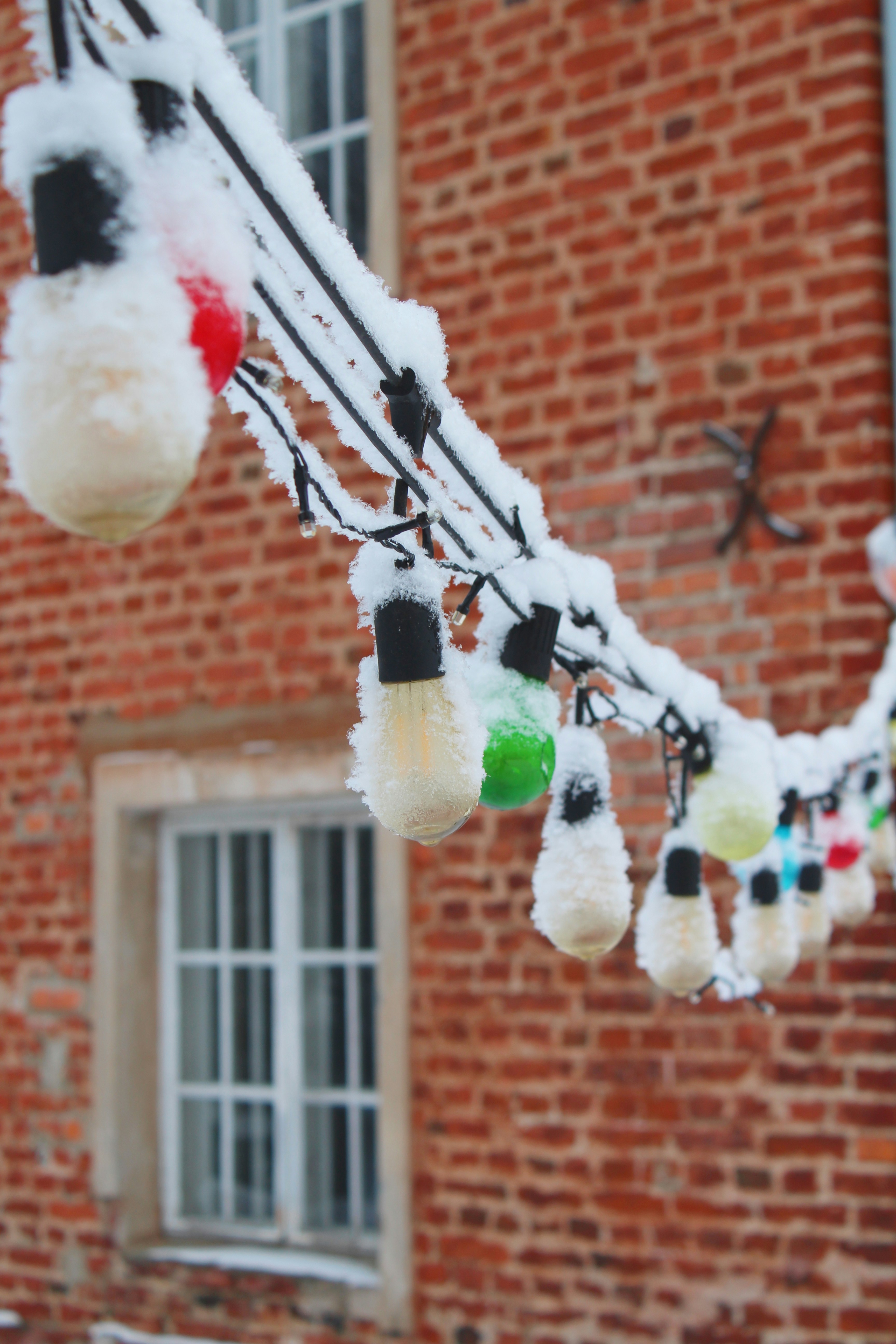 String lights covered in snow hang outside brick building.