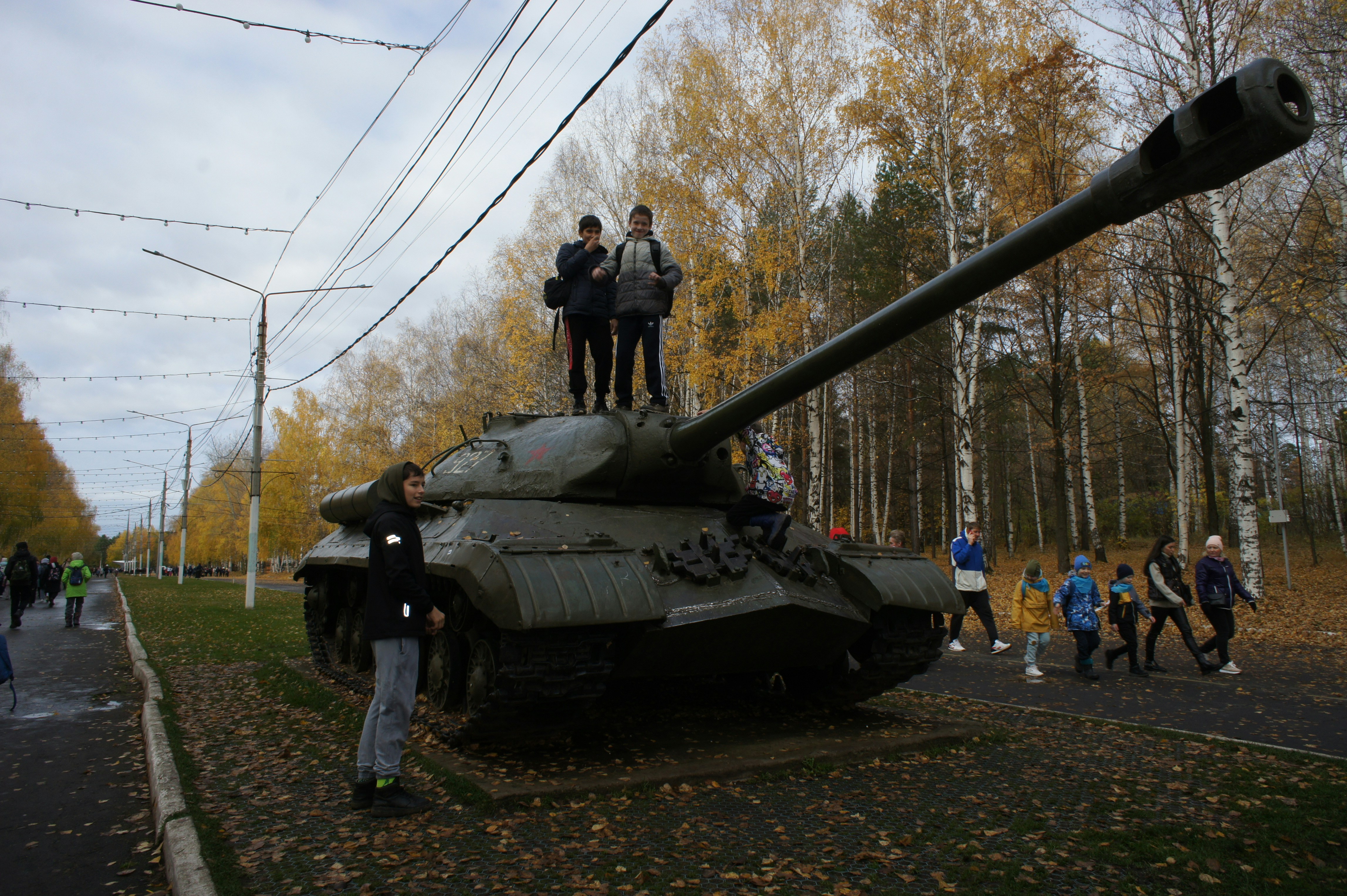 People stand on and around a military tank outdoors.