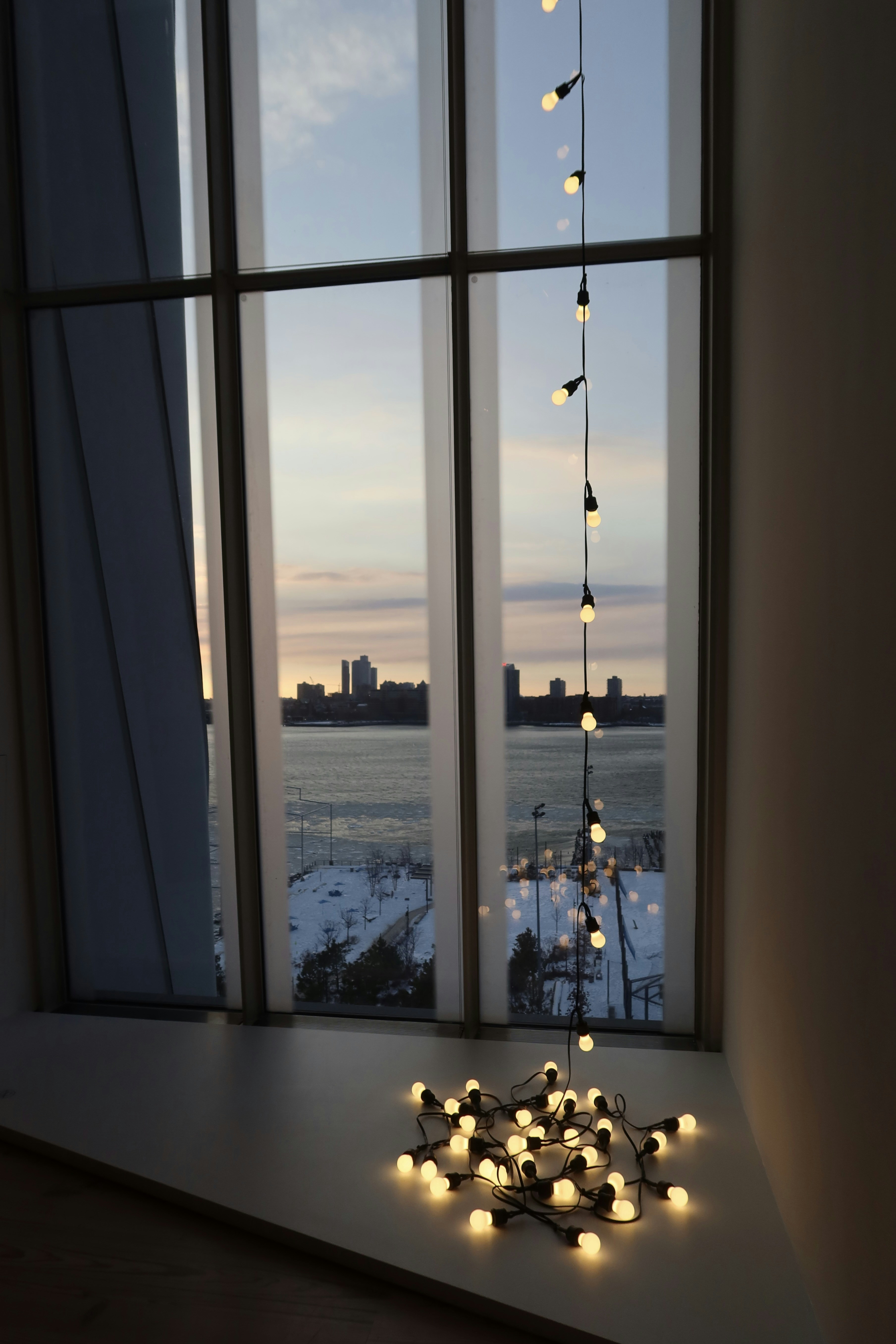 String lights drape down from a large window overlooking water.
