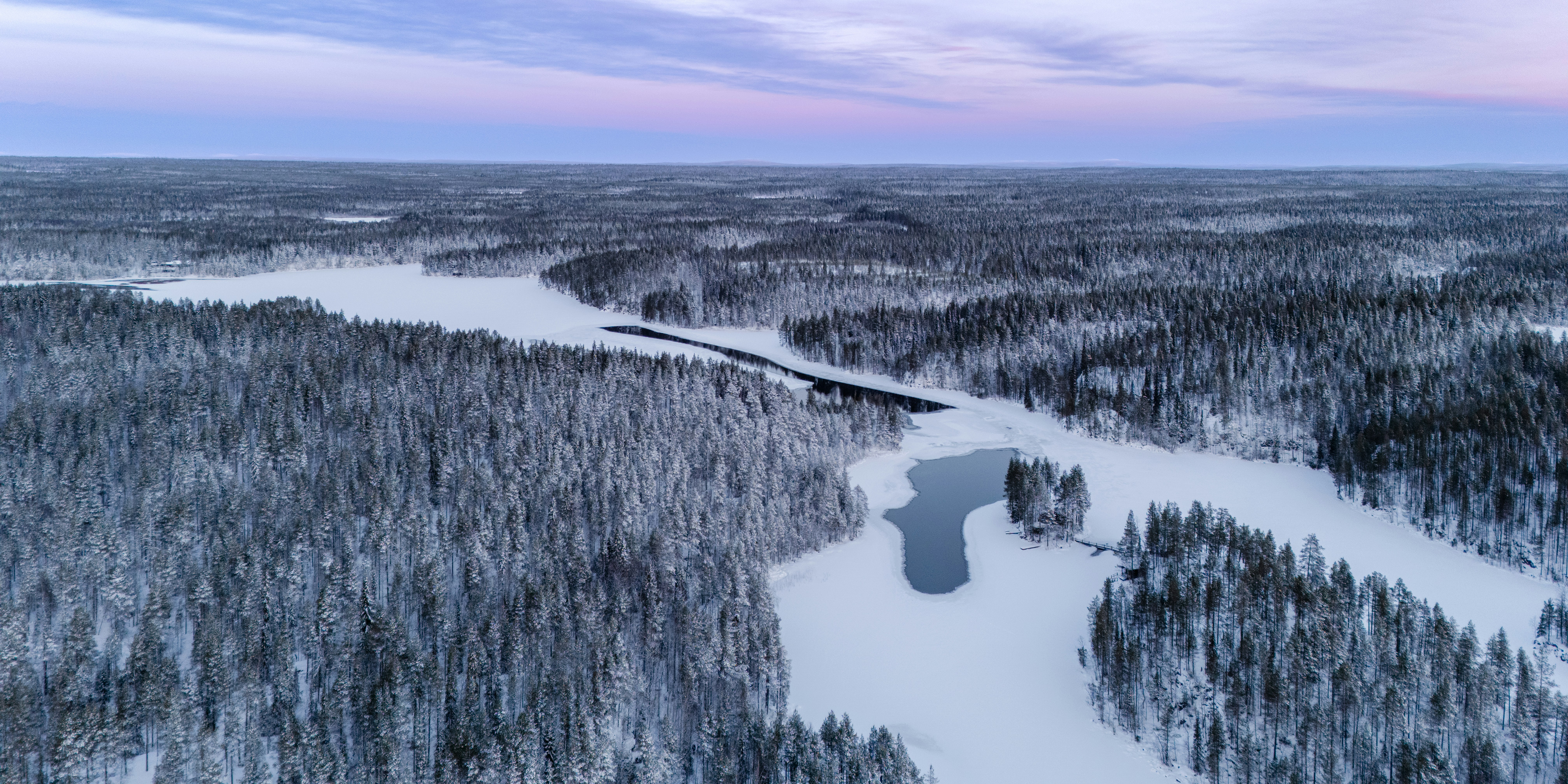 Schneebedeckte Waldlandschaft mit einem zugefrorenen Fluss und einer Brücke.