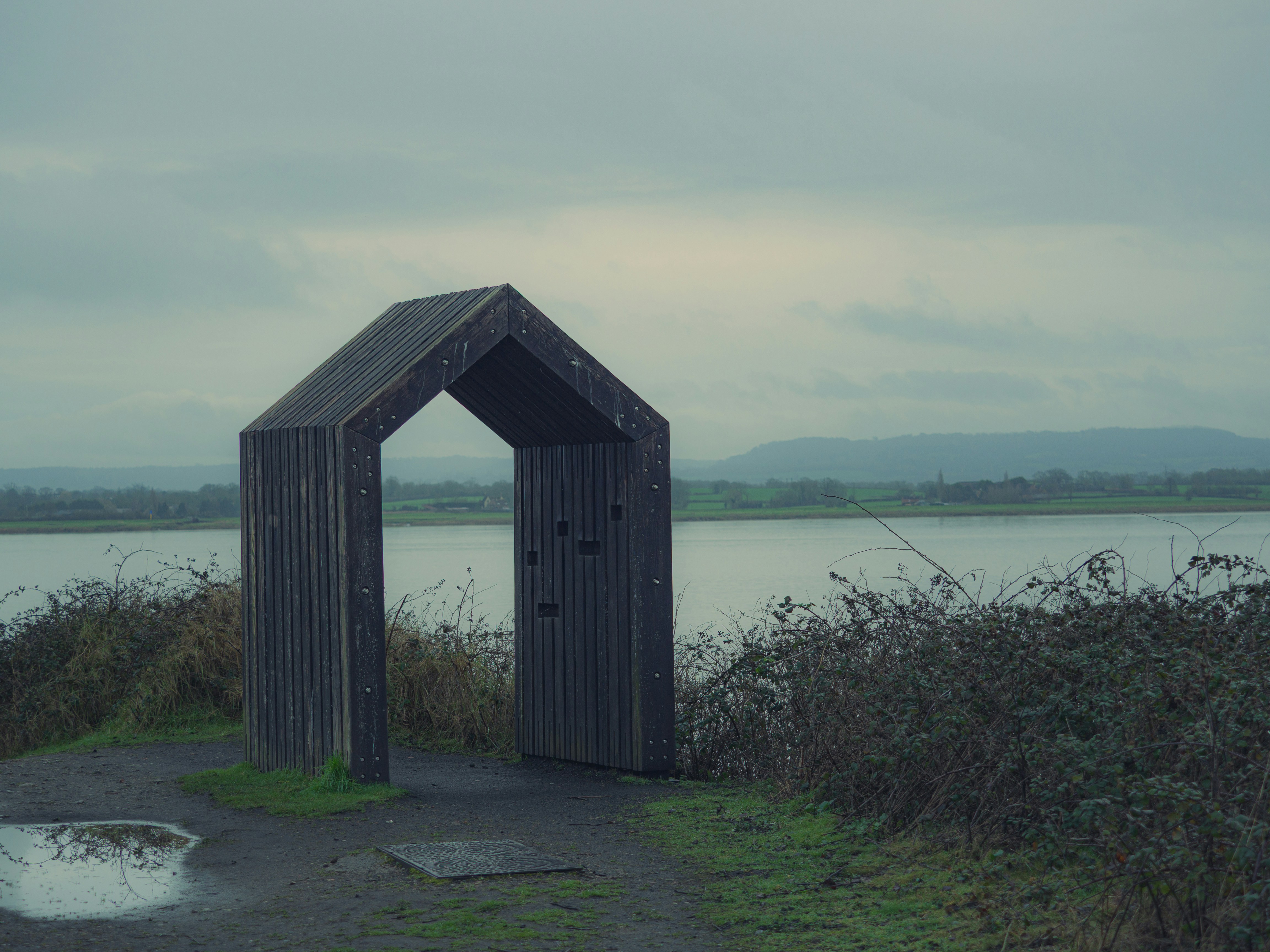 Wooden archway by a calm lake under cloudy sky