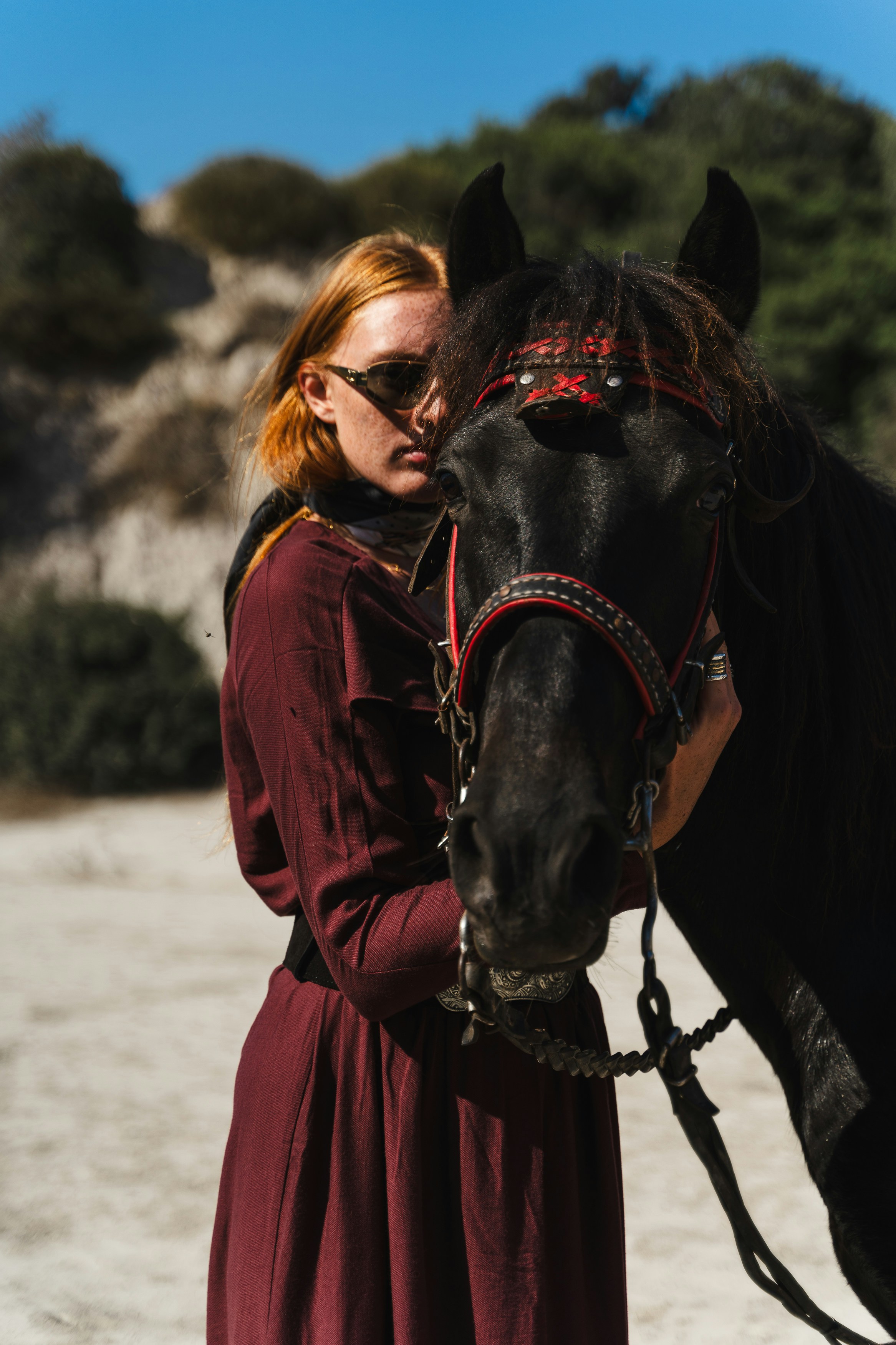 Woman with sunglasses embraces a black horse