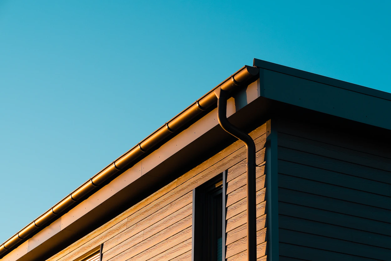 A dark gutter and downspout on a modern home with wood siding