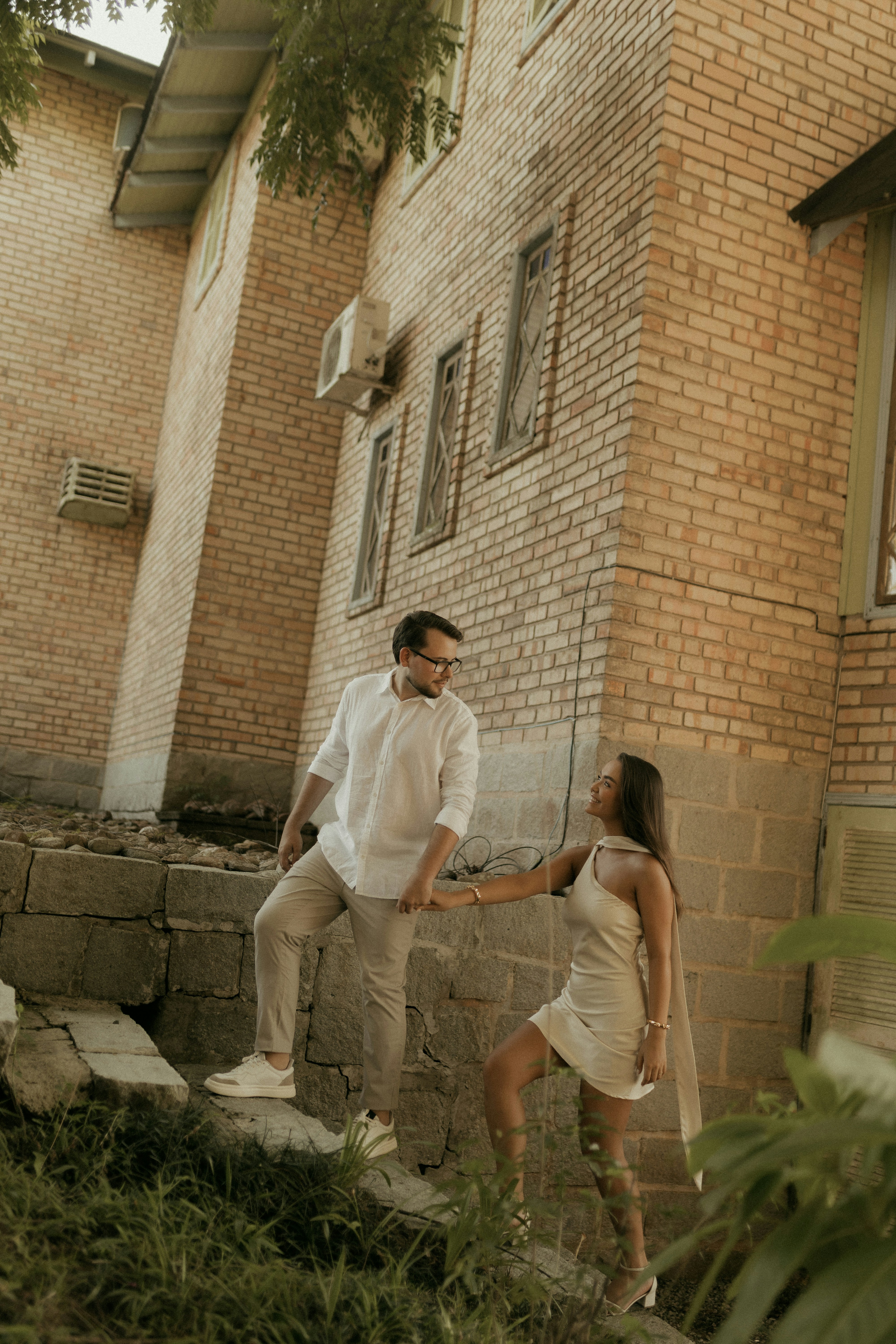 Couple se tenant la main sur des escaliers extérieurs près d’un bâtiment en brique
