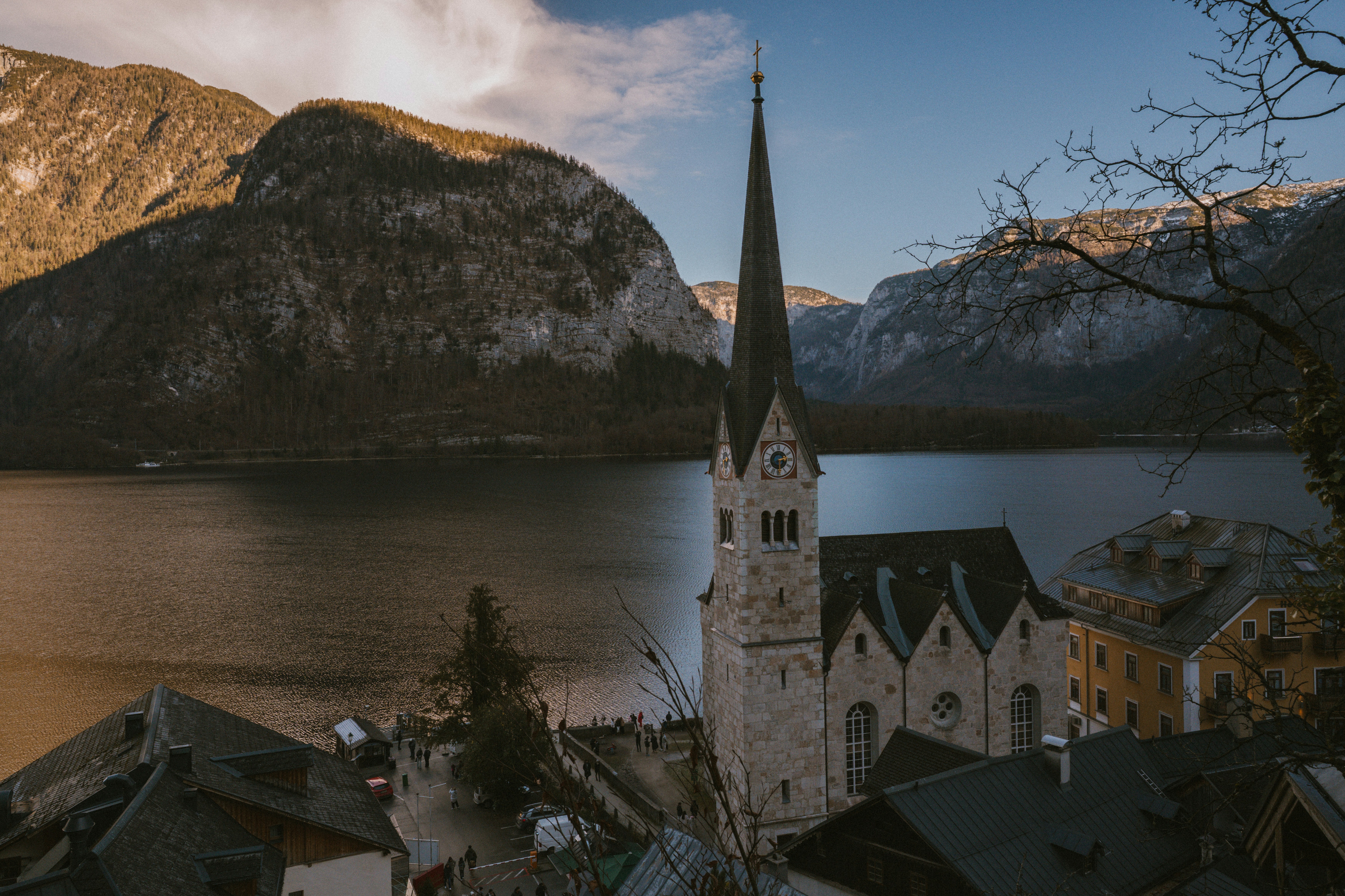 Church steeple rises above a lakeside village with mountains.