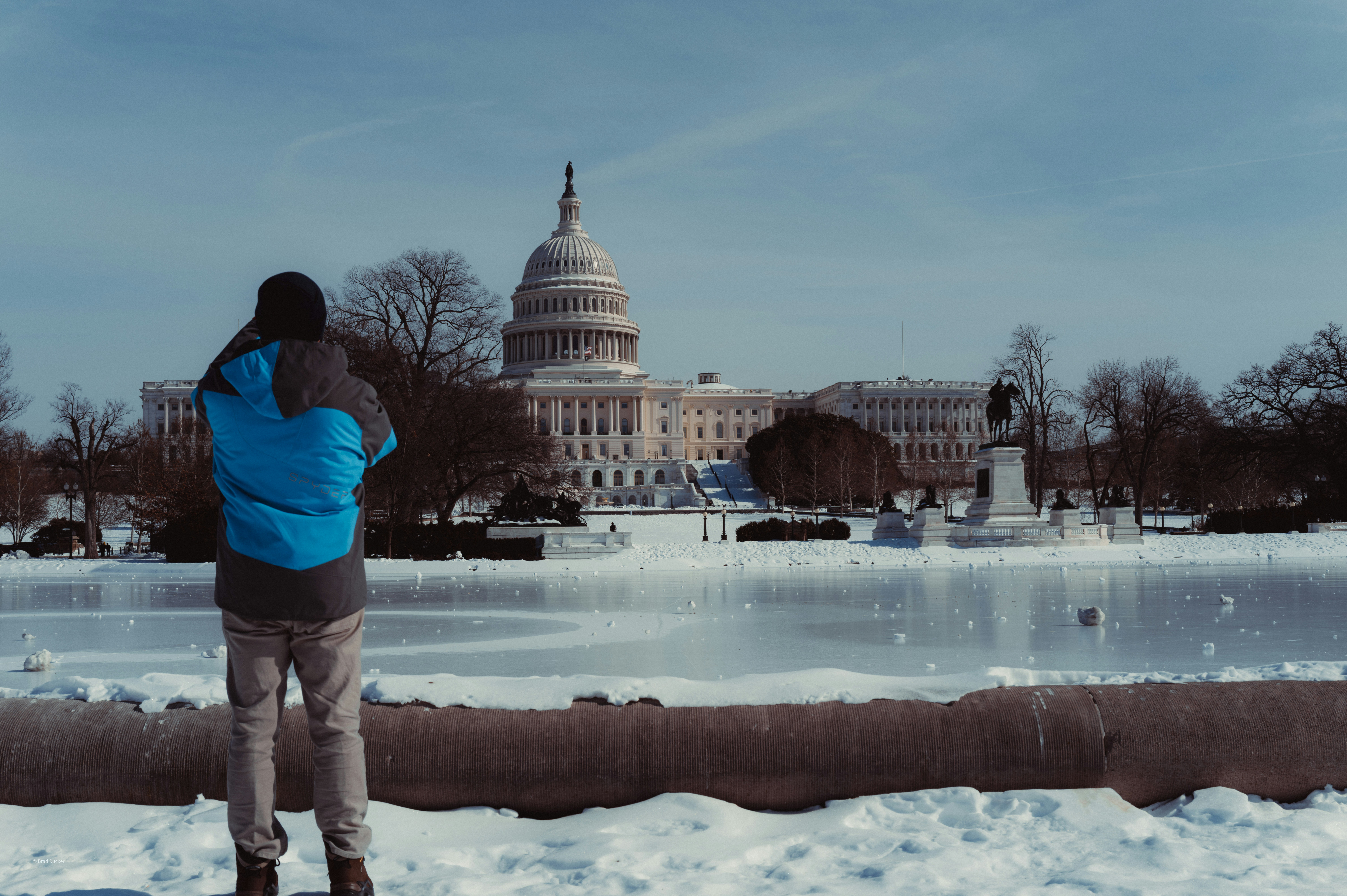 A stack of dusty files piled high on a desk in a dimly lit government office, with a blurry calendar showing past dates, symbolizing pending work.