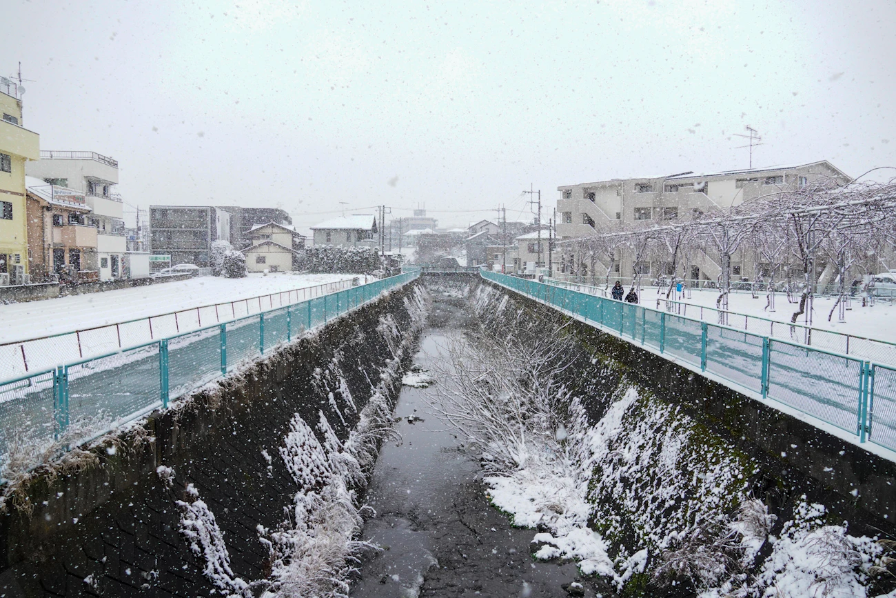 雪の日の川沿いに並ぶ都市の住宅地