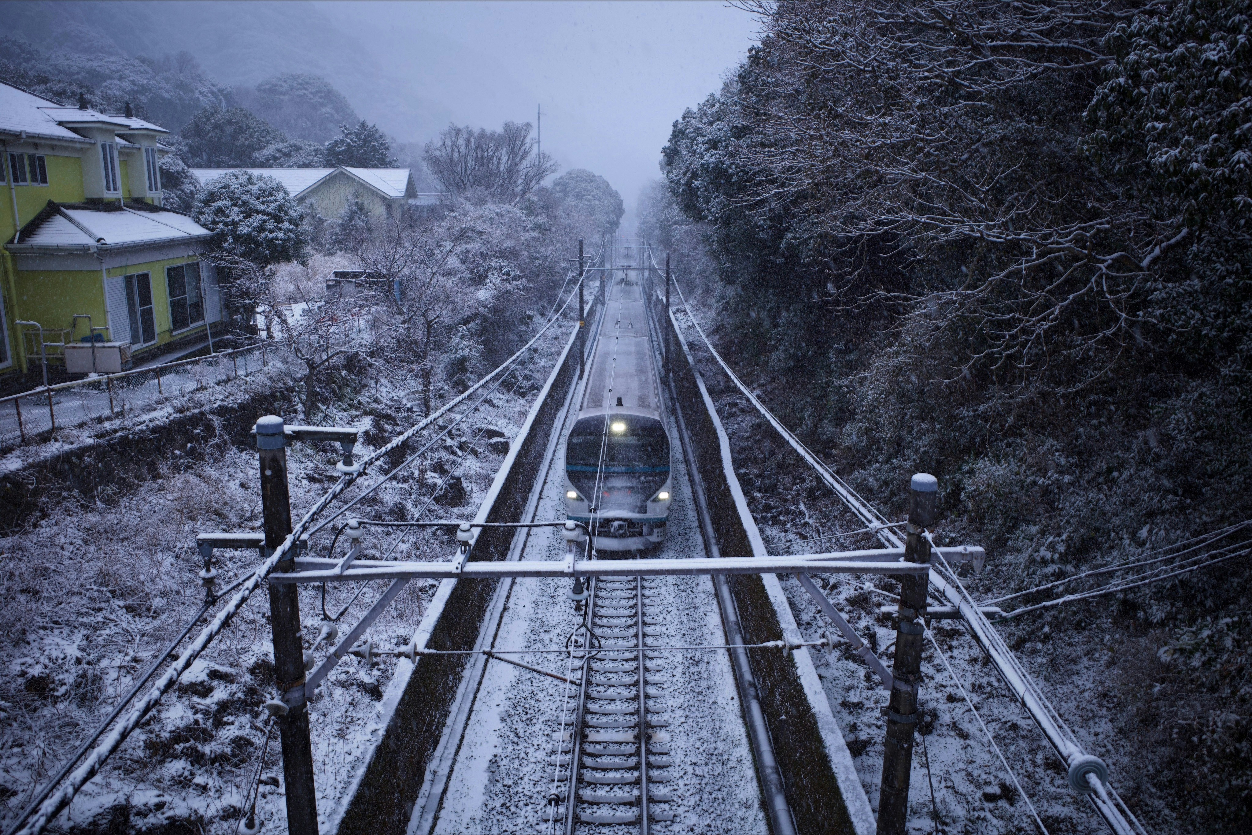 A train travels on snowy tracks through a wooded area.