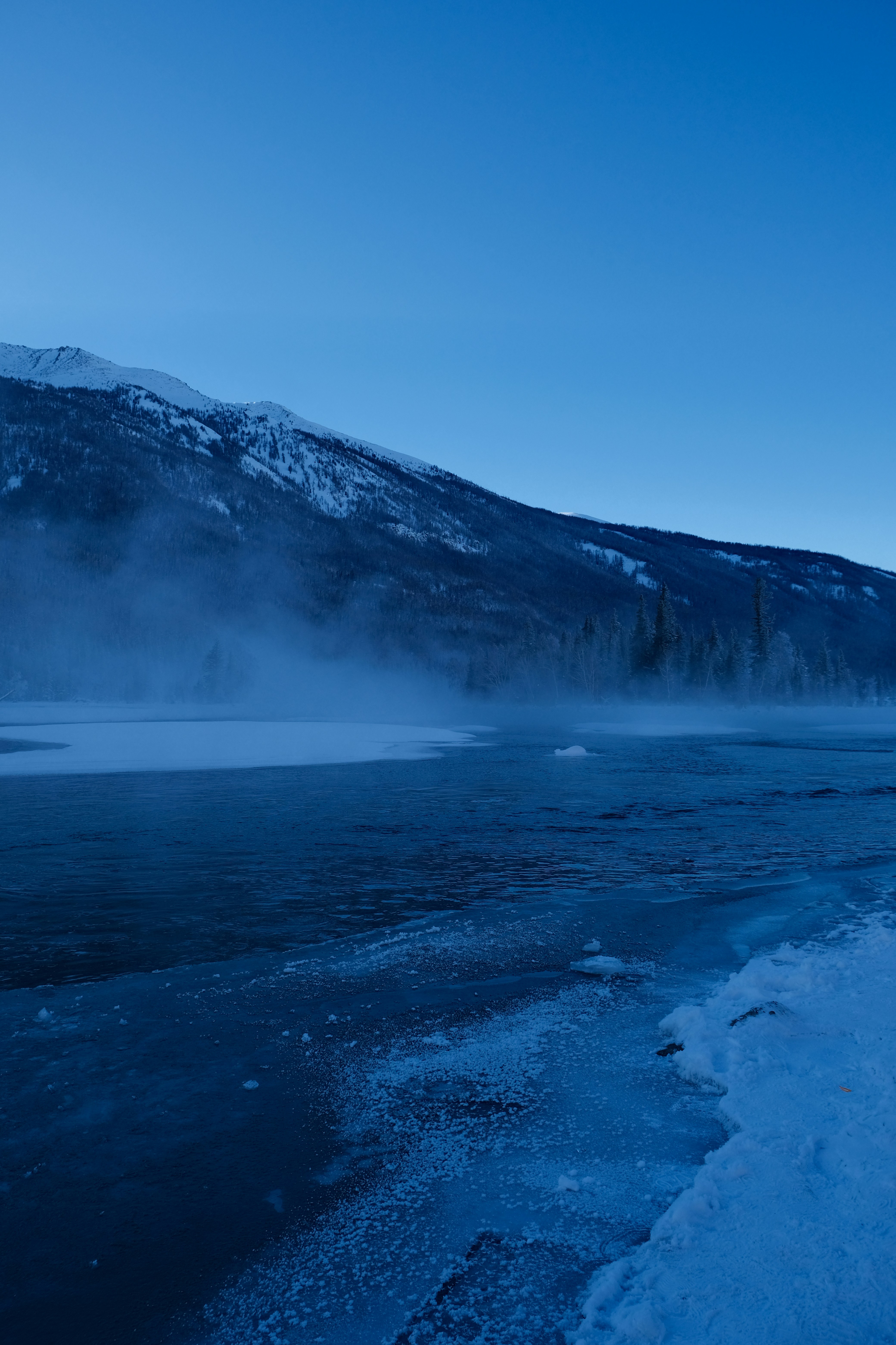 Orilla brumosa con montañas cubiertas de nieve bajo cielo despejado