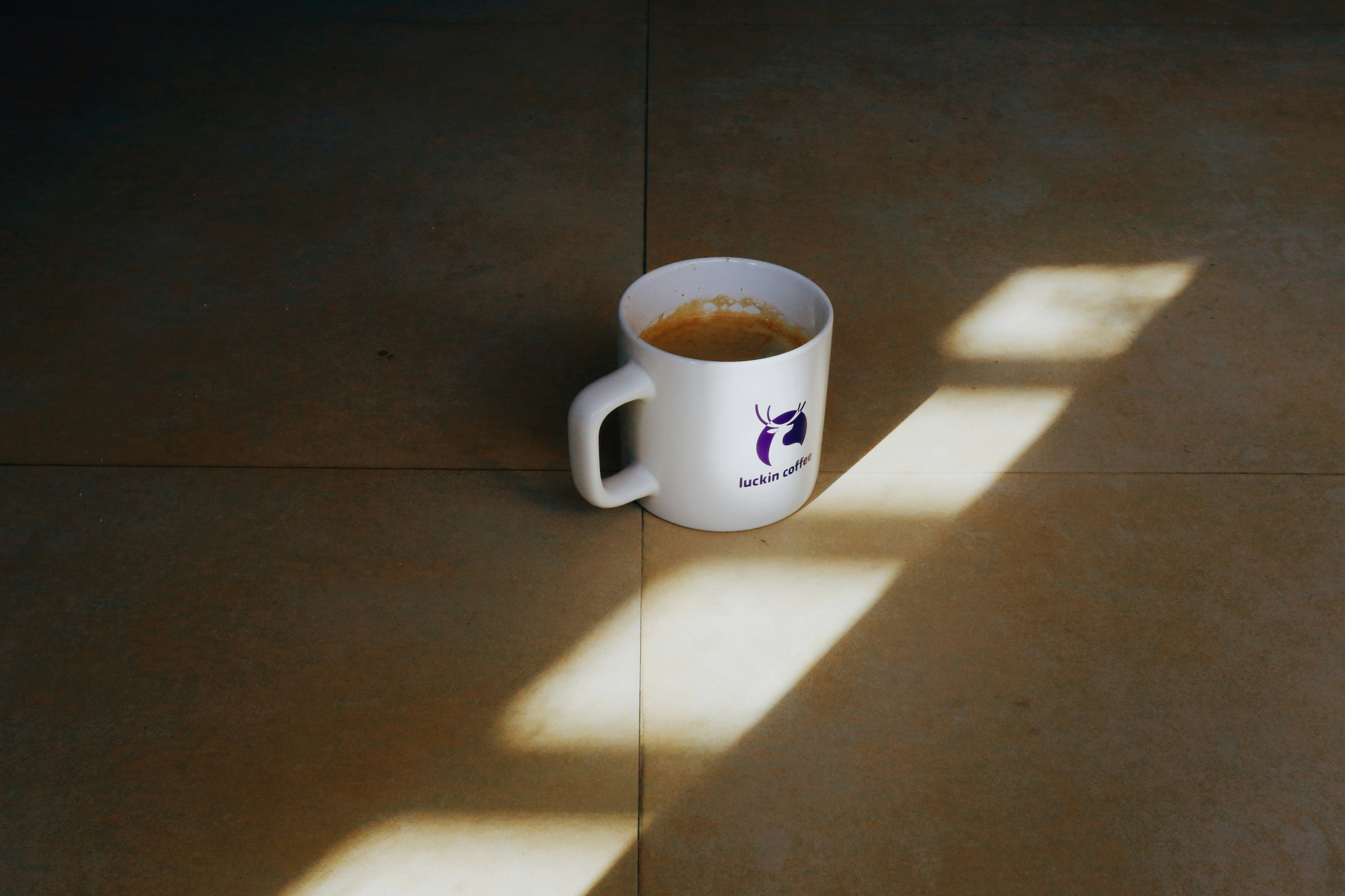 A white mug filled with coffee sits on a floor.