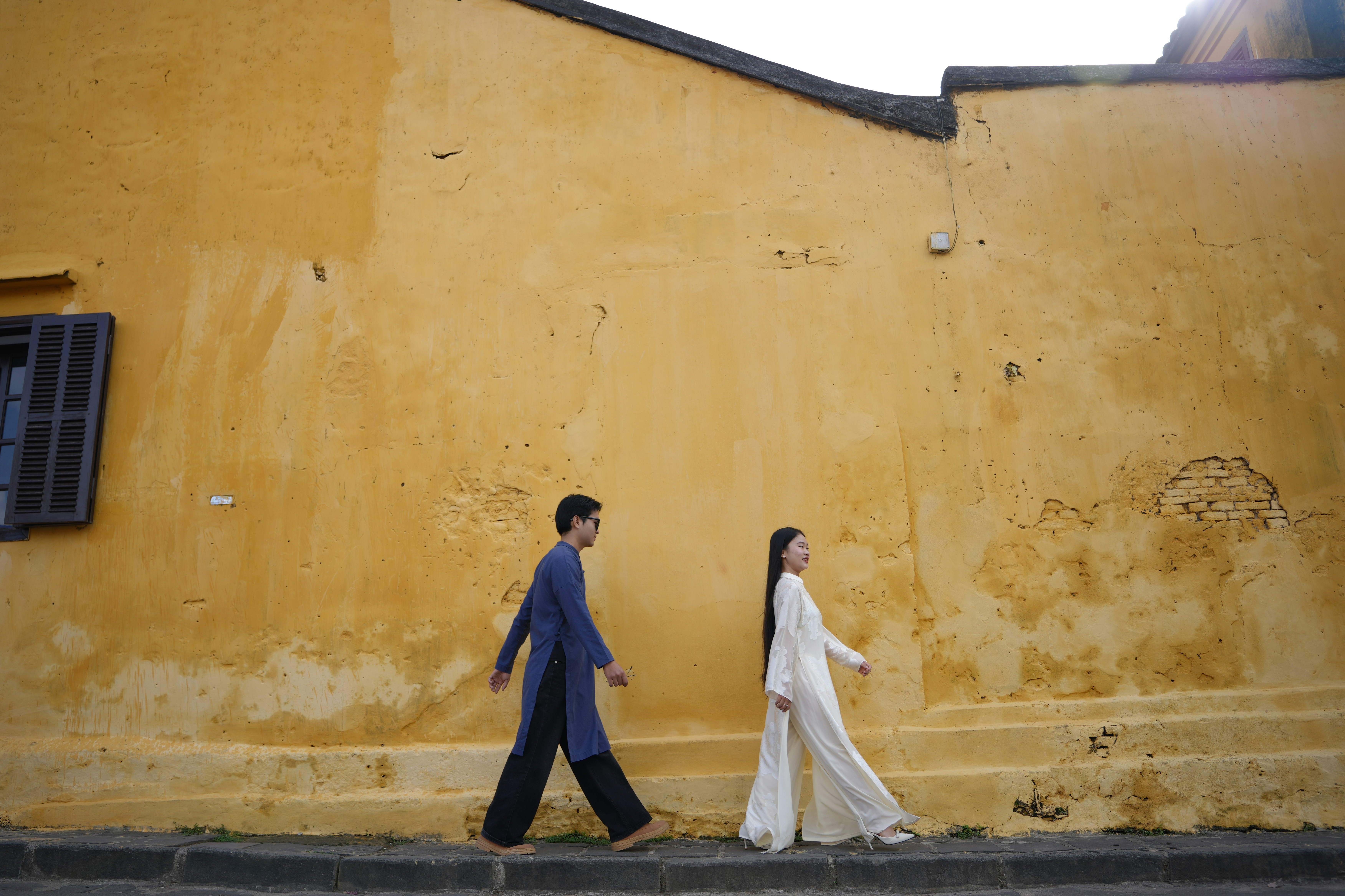 A couple walks along a yellow wall