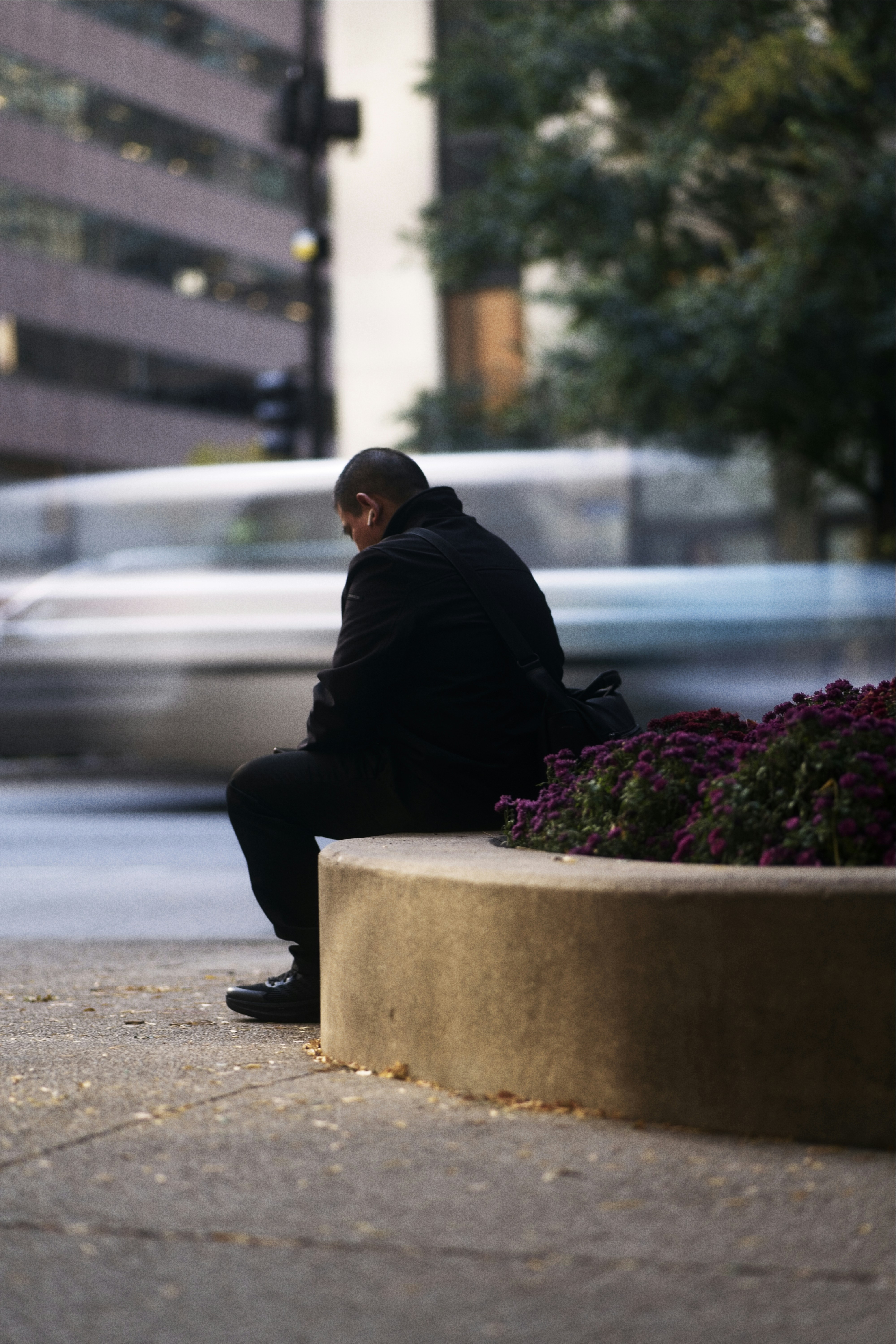 Man in black coat sits on concrete bench in city