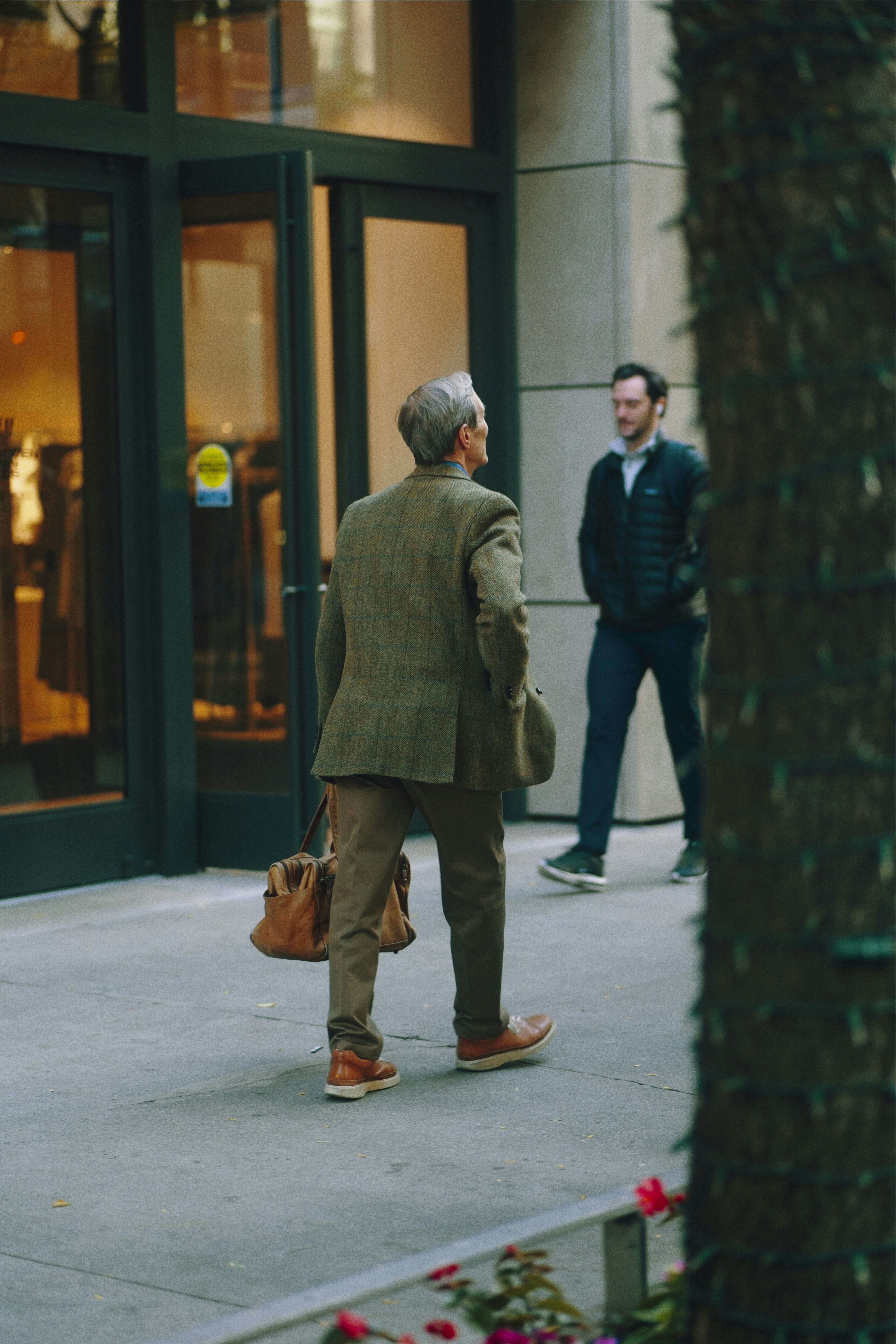 Man in tweed jacket walks past store entrance.