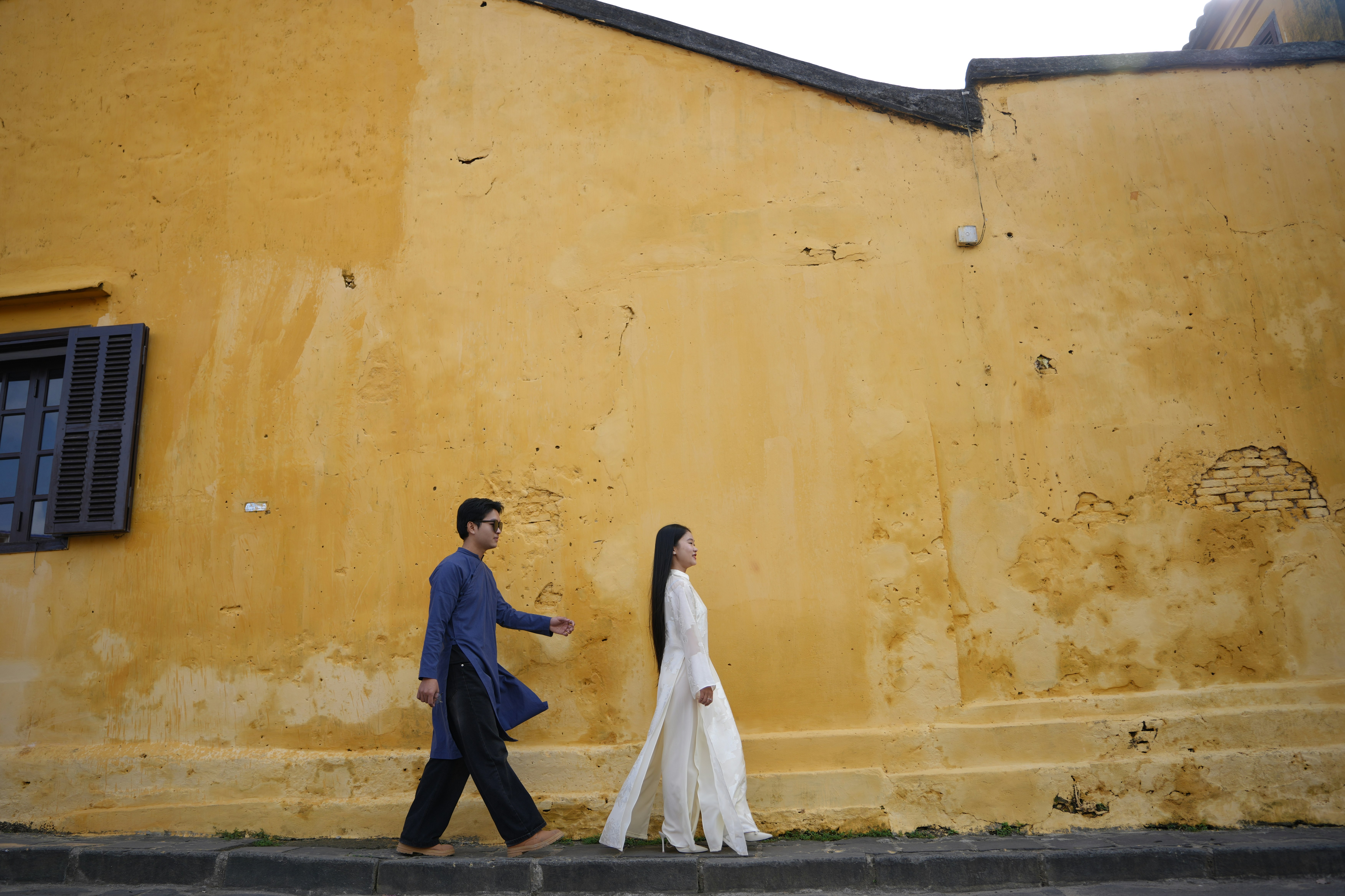 Couple in traditional clothing walks along yellow wall