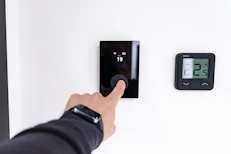 Finger adjusting a modern digital thermostat on wall