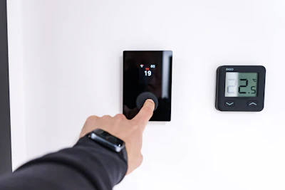 Finger adjusting a modern digital thermostat on wall