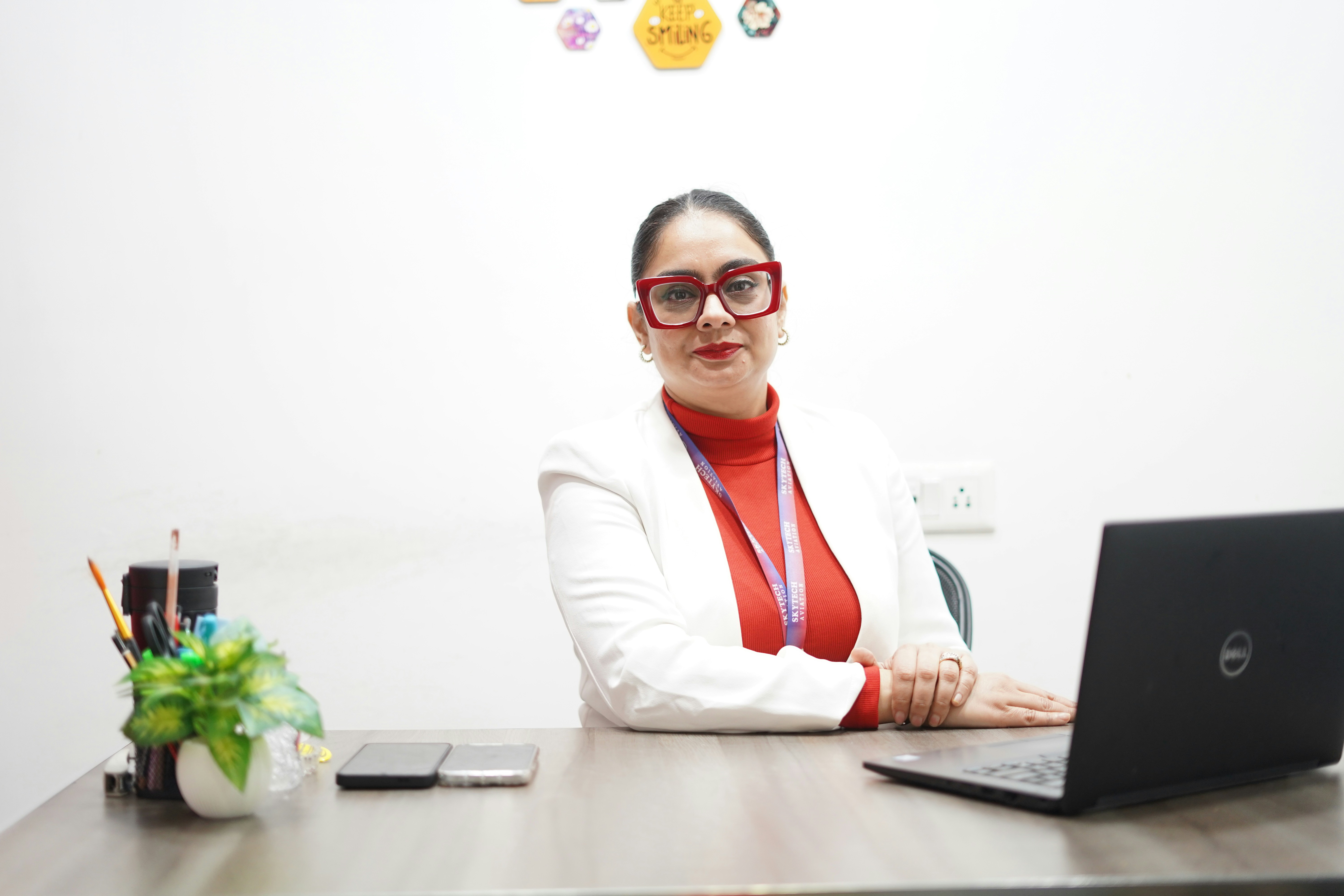 A woman in a white blazer sits at a desk.