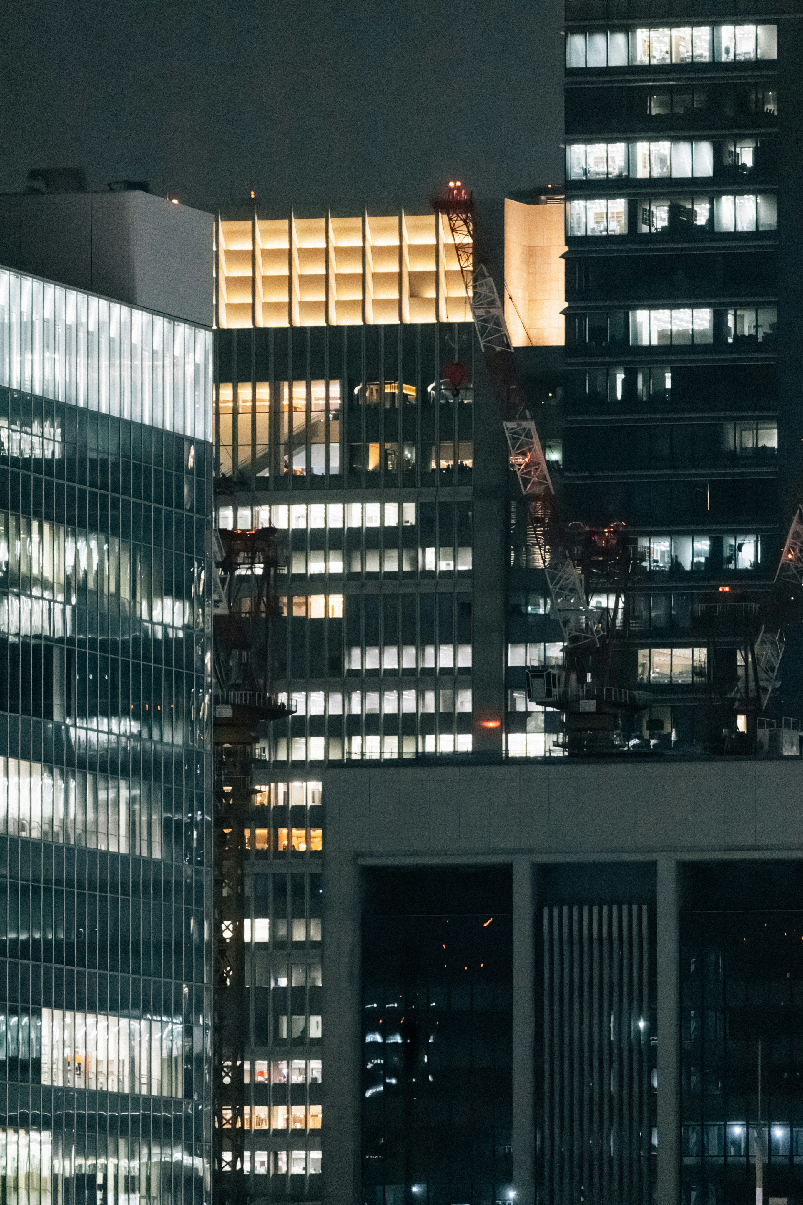 Modern skyscrapers illuminated at night with cranes visible.