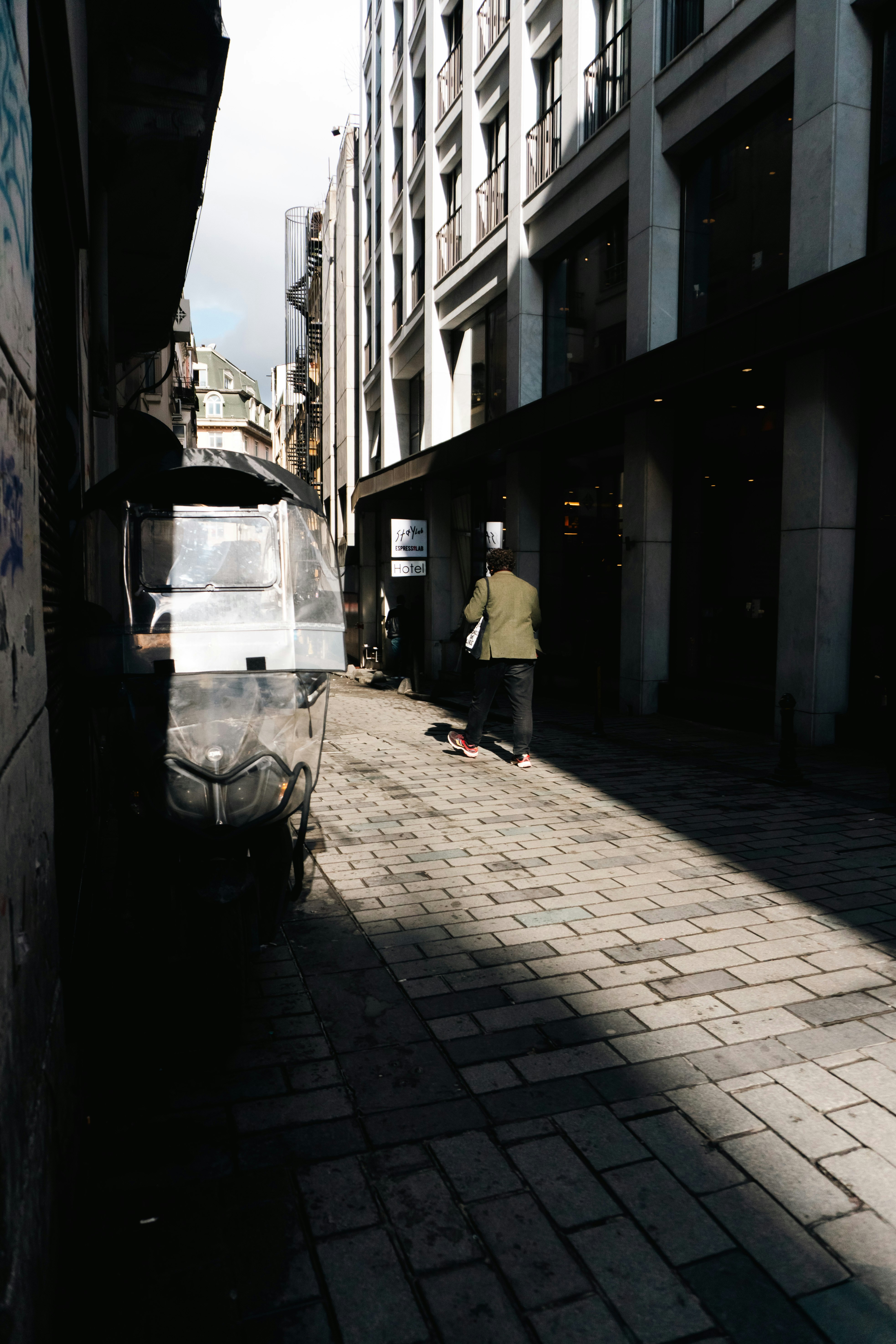 Man walks down sunlit cobblestone alleyway with cart.