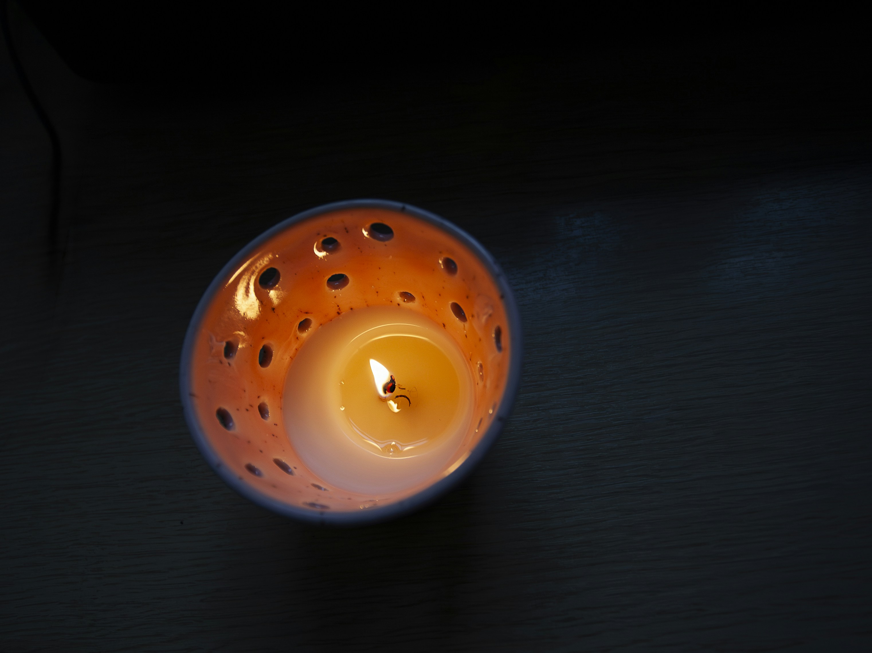 A lit candle in an orange, perforated holder.