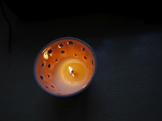 A lit candle in an orange, perforated holder.