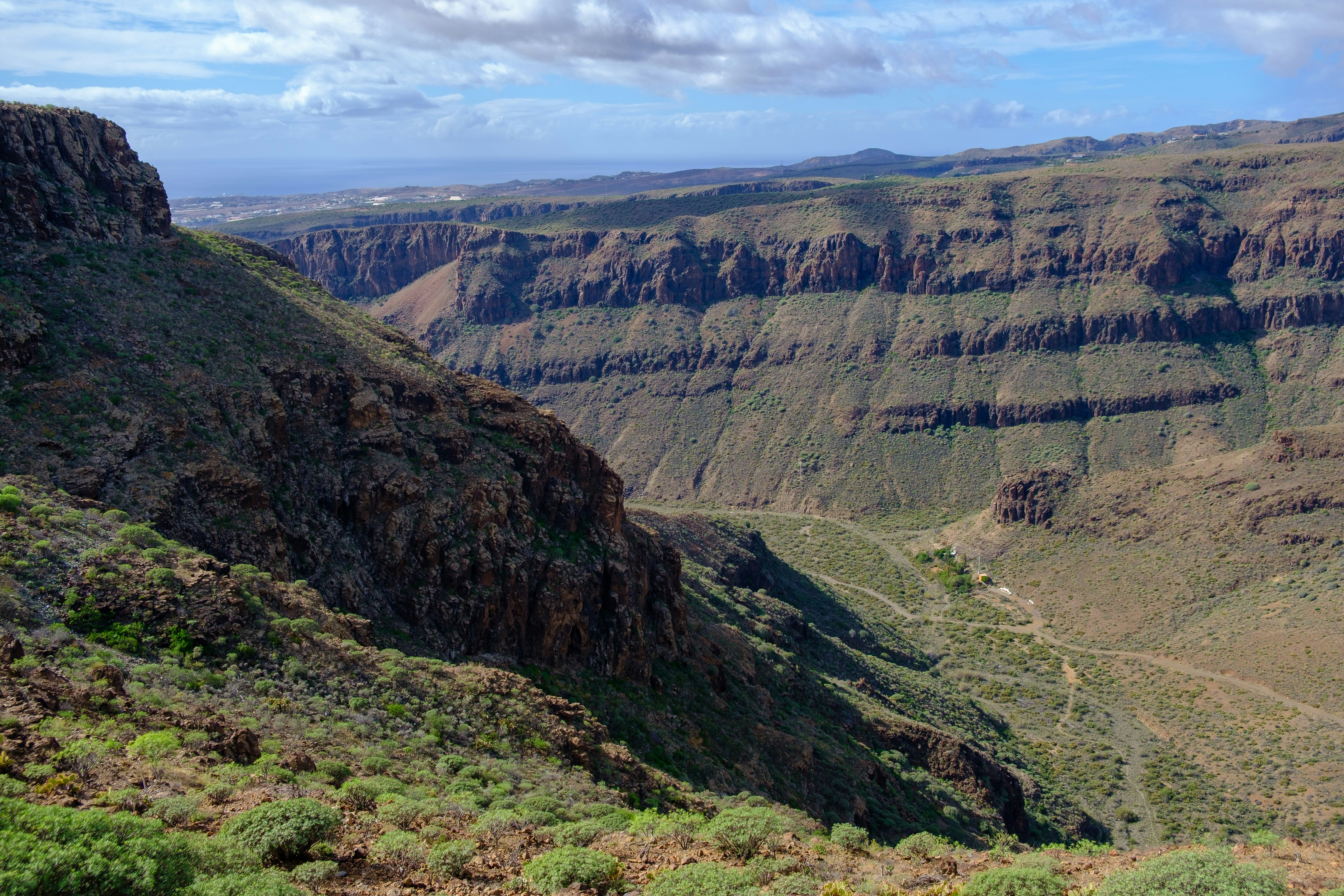 Rugged canyon landscape with sparse vegetation under a cloudy sky.