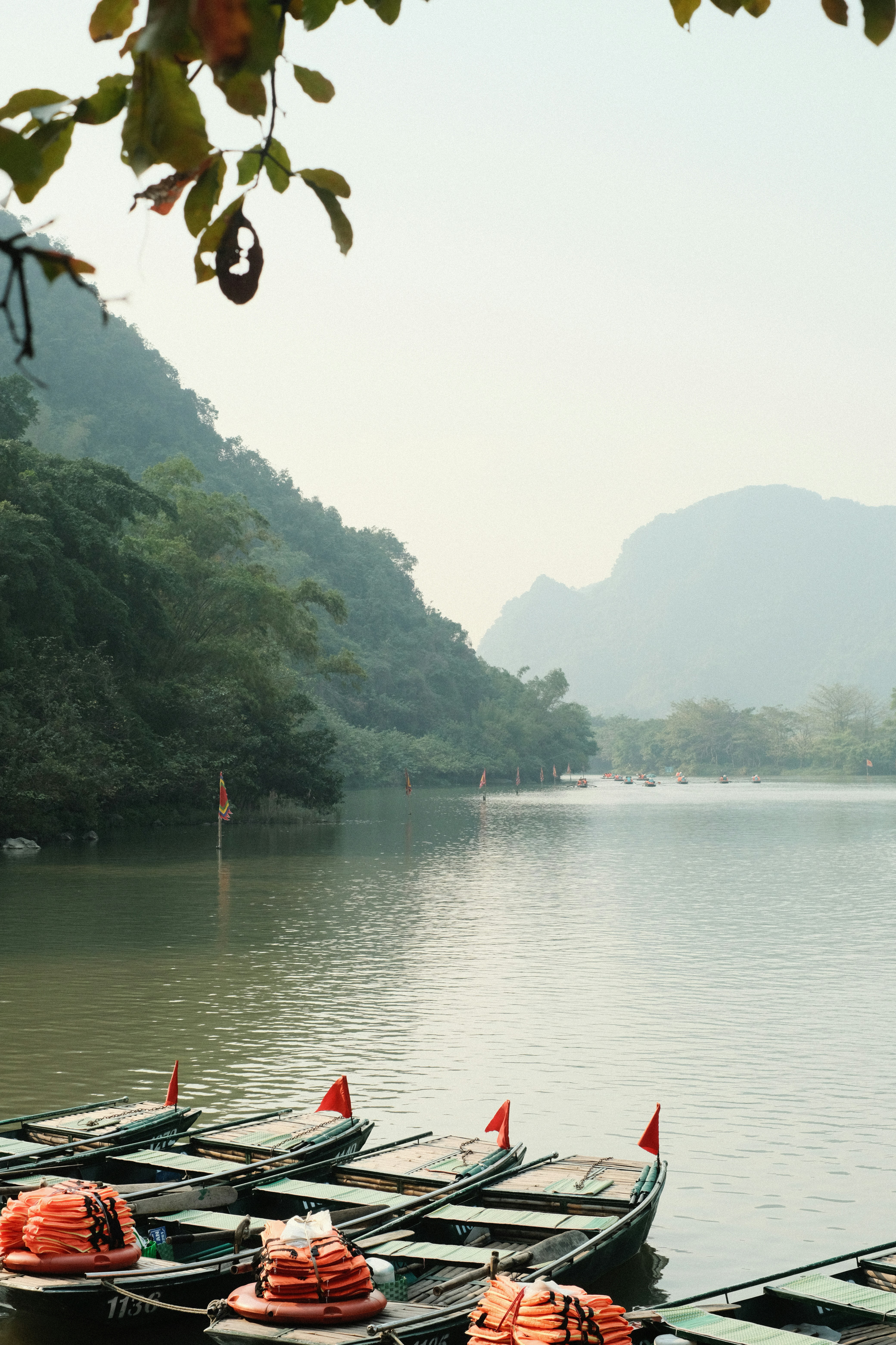 Small boats with red flags float on a calm lake.