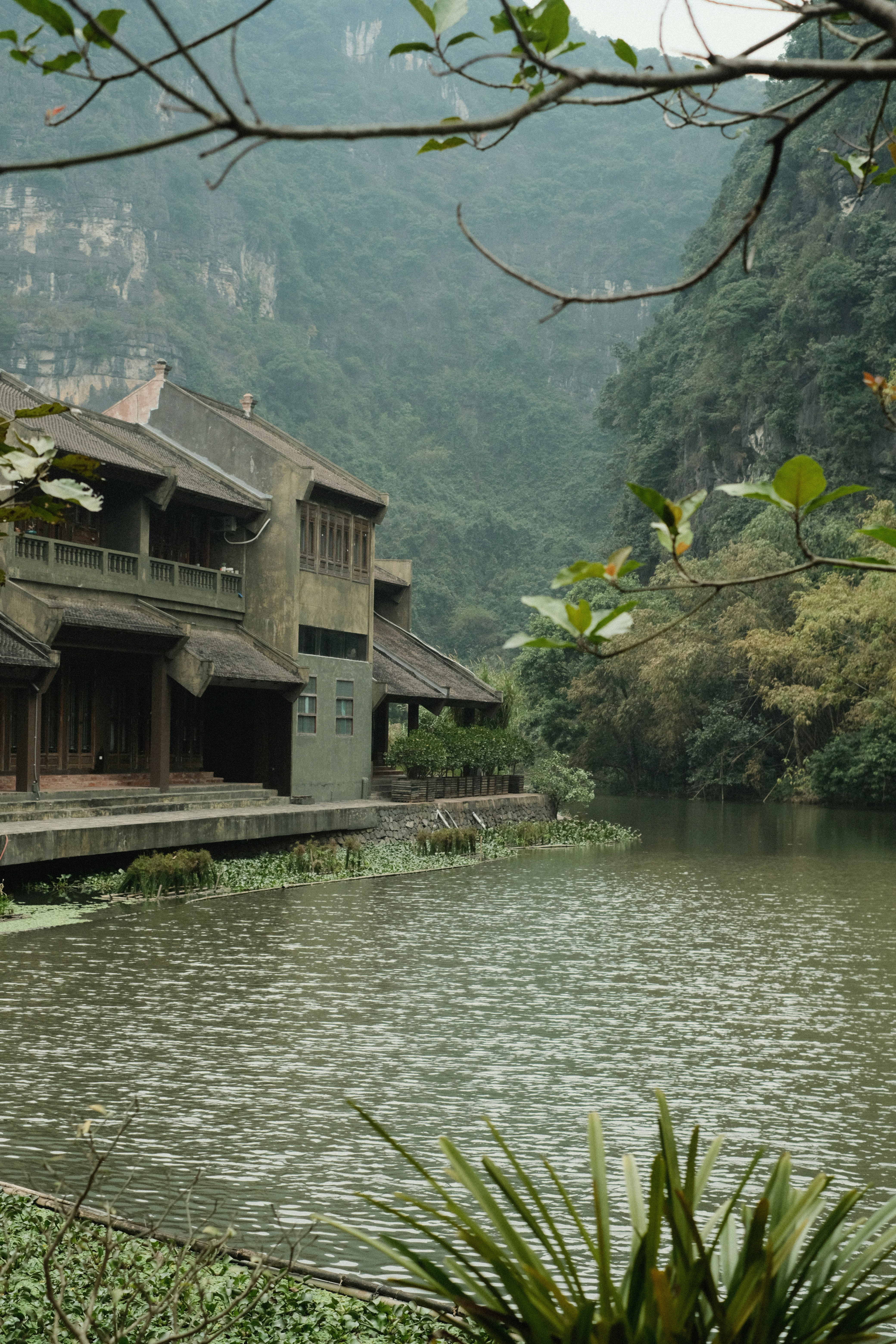 Traditional building beside a calm river and mountains.