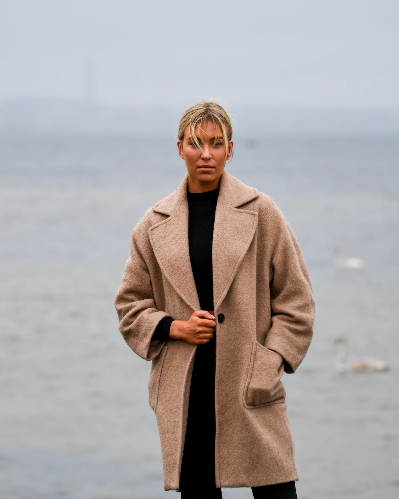 A woman in a tailored camel coat standing by the sea