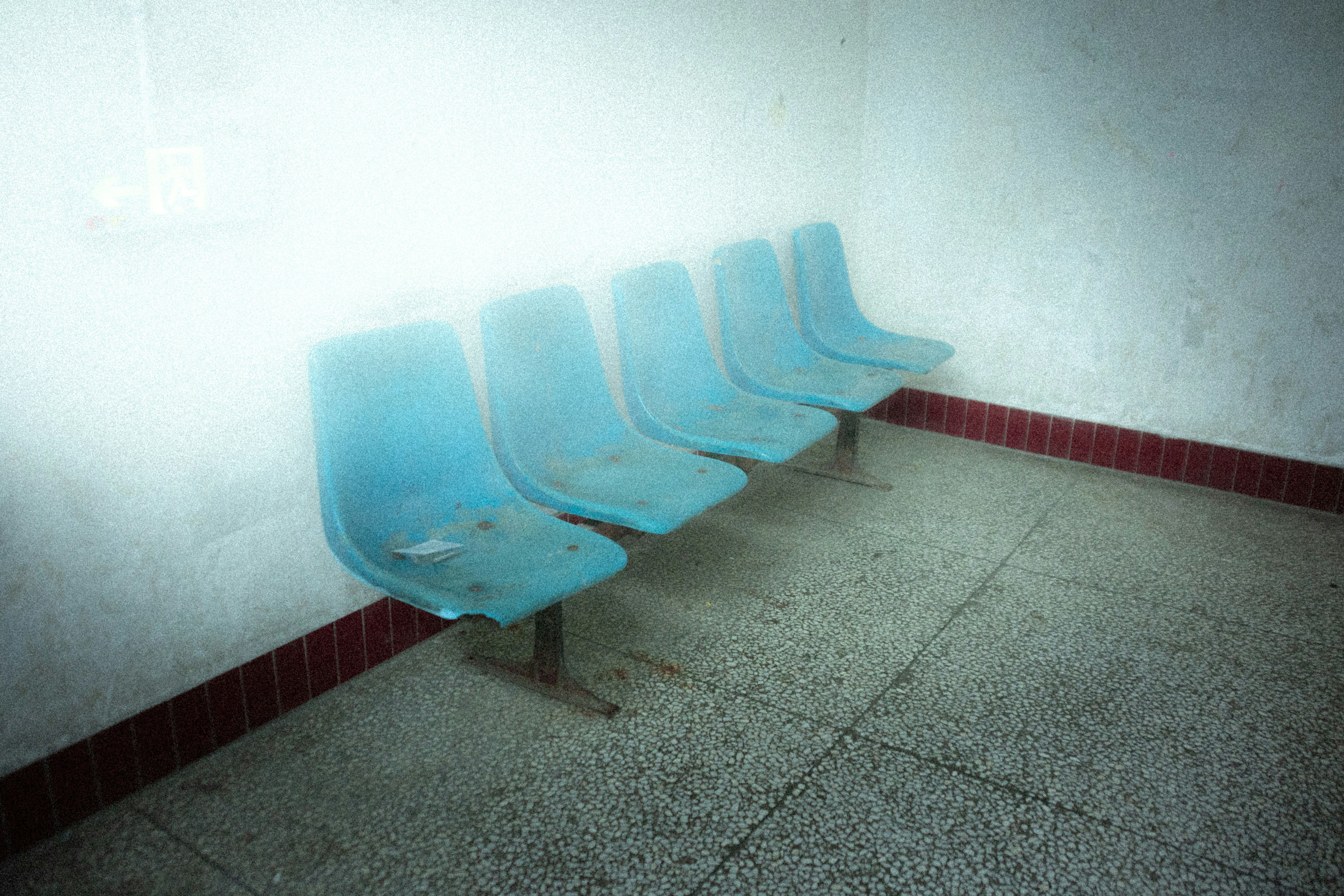 Row of empty blue plastic chairs in a waiting room.
