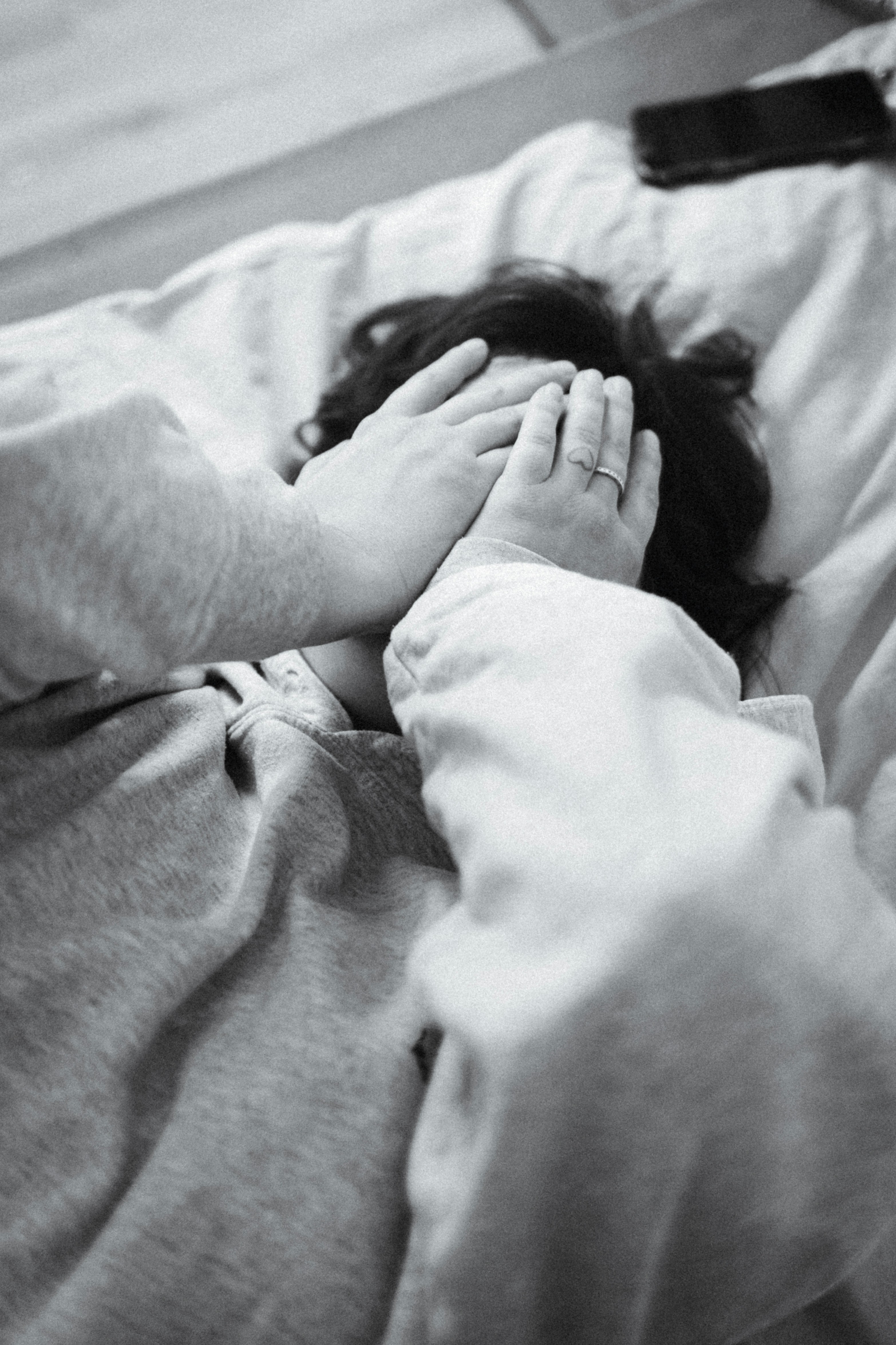 Child covers face with hands while lying in bed.
