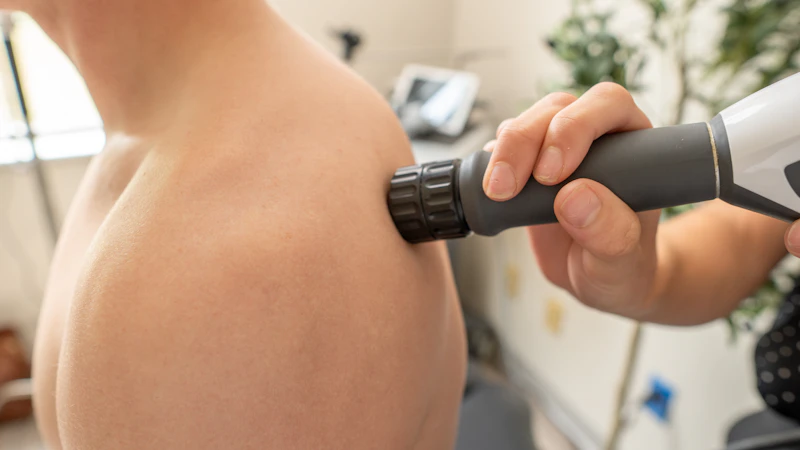Therapist treating a painful shoulder with a hand-held therapy device