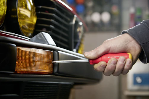 Hand using screwdriver to fix car bumper