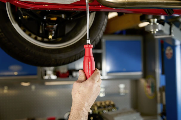 Mechanic's hand using screwdriver on car underside.