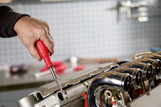 Mechanic uses screwdriver to fix car engine part.