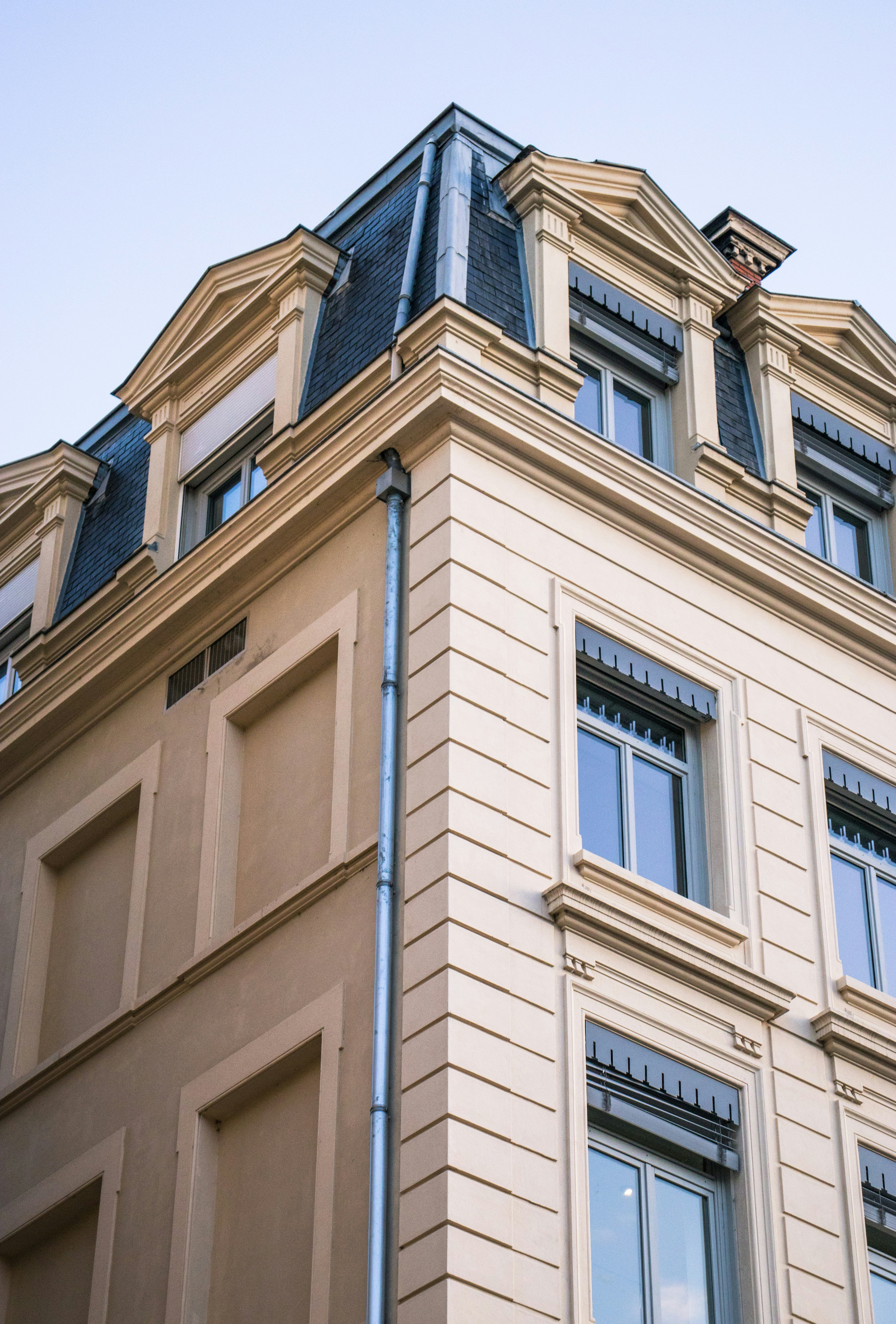 Corner of a beige building with mansard roof.
