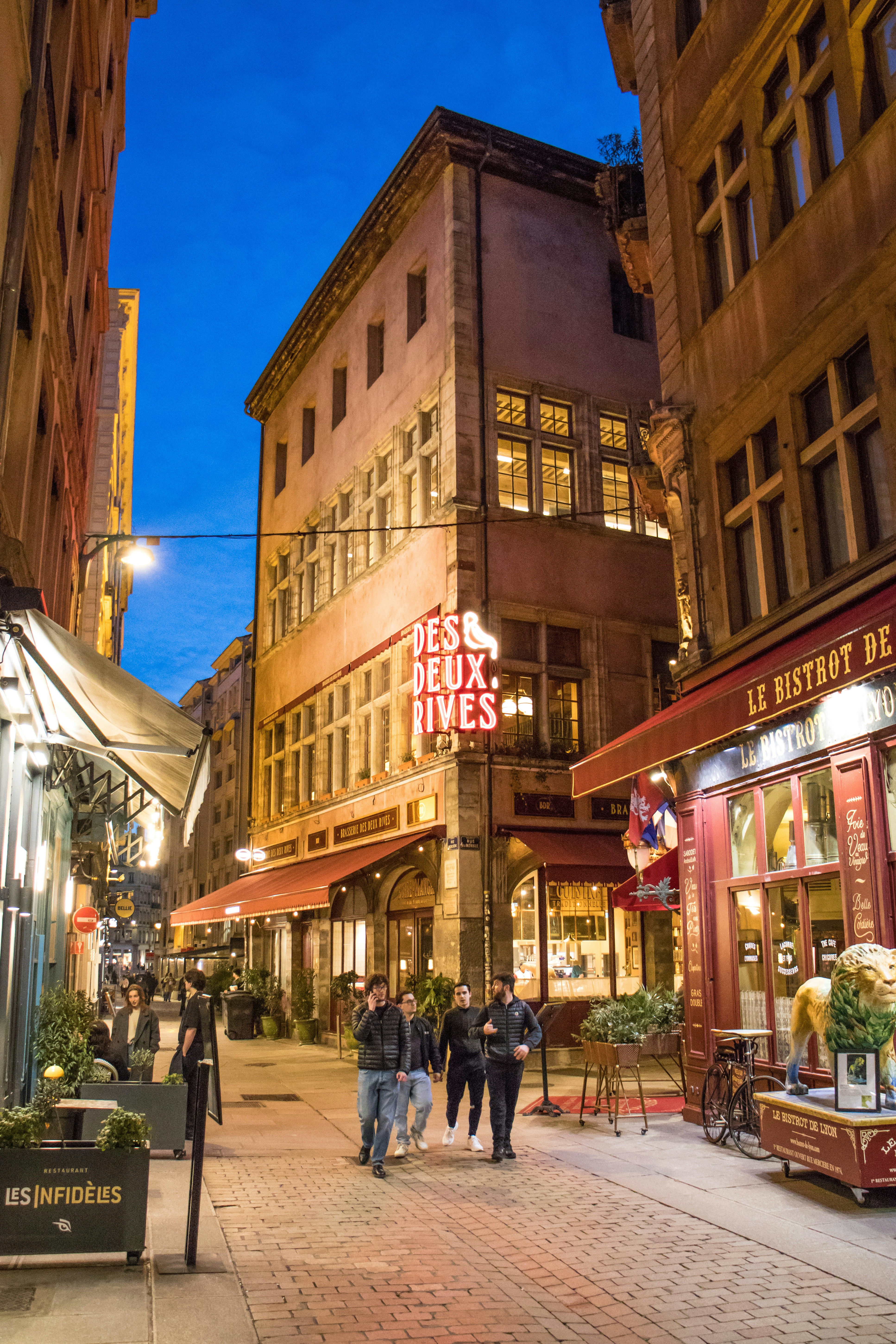 People walking down a narrow street with illuminated buildings.