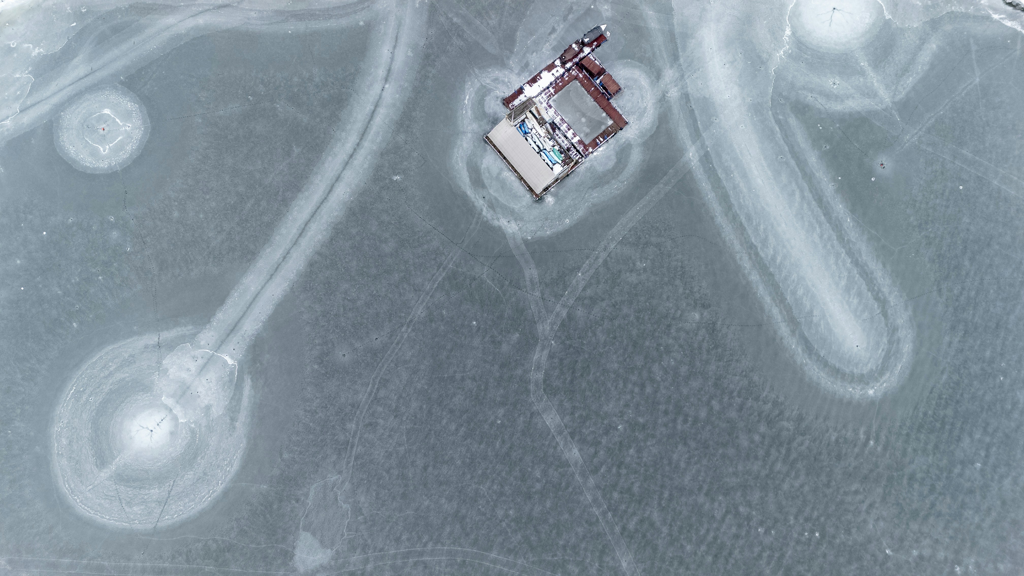 Vue aérienne d’un petit bâtiment au bord d’un lac gelé.