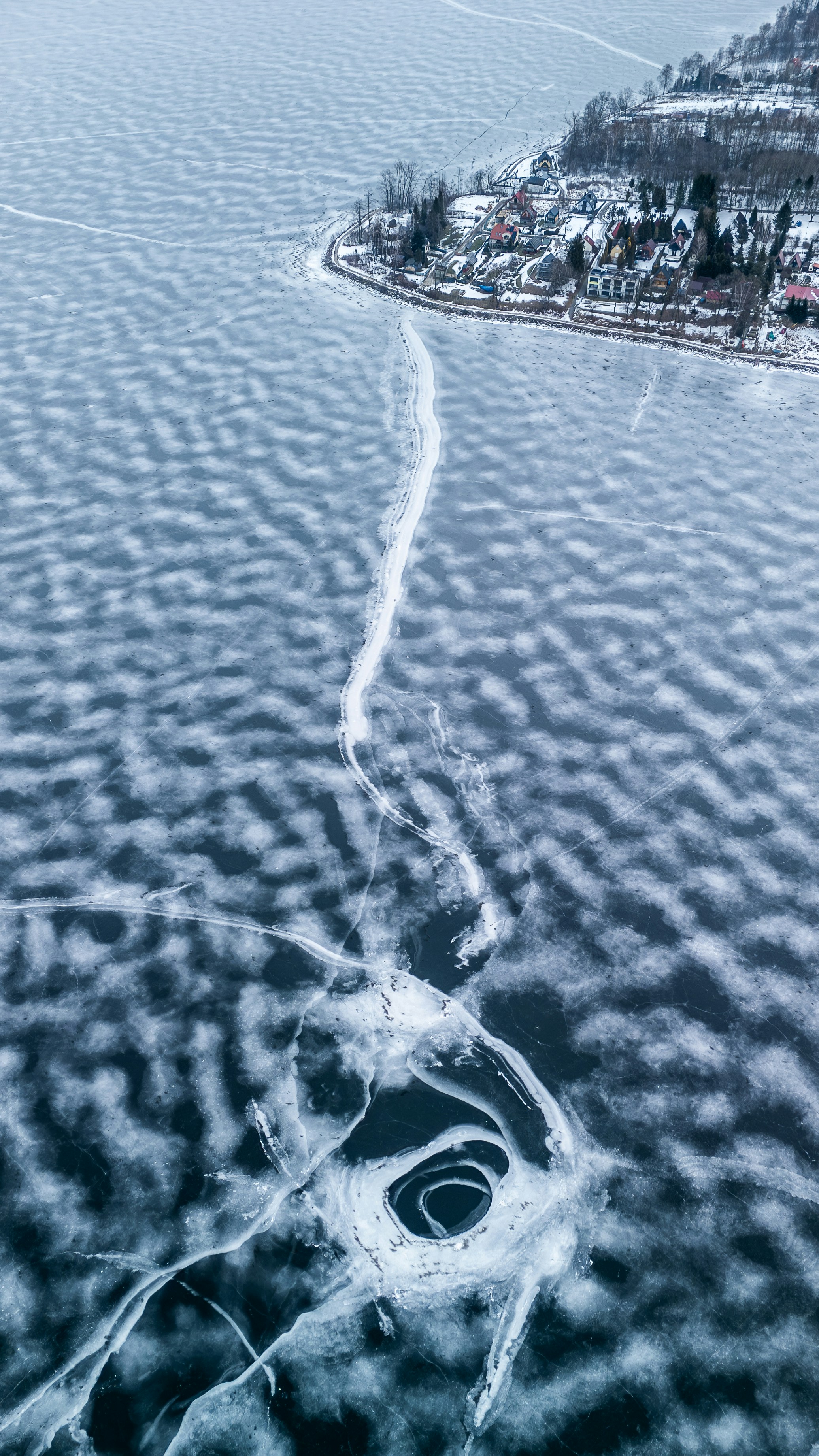 Frozen lake with intricate ice patterns and a distant village.