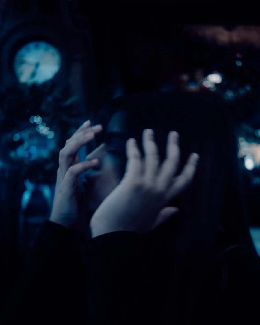 A person covering their face with both hands in a dark room, a picture of anxiety