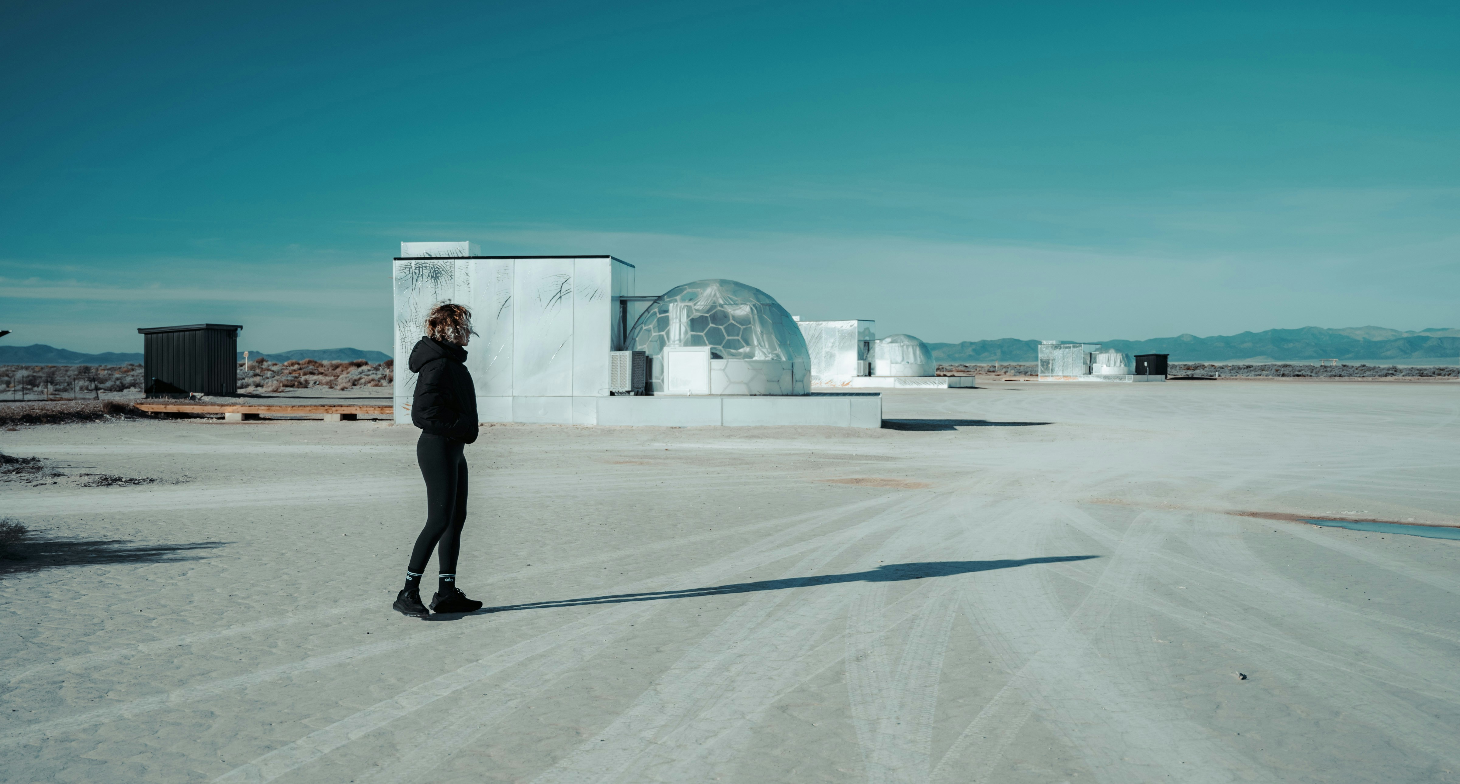 Woman standing in a desolate landscape with modern buildings.