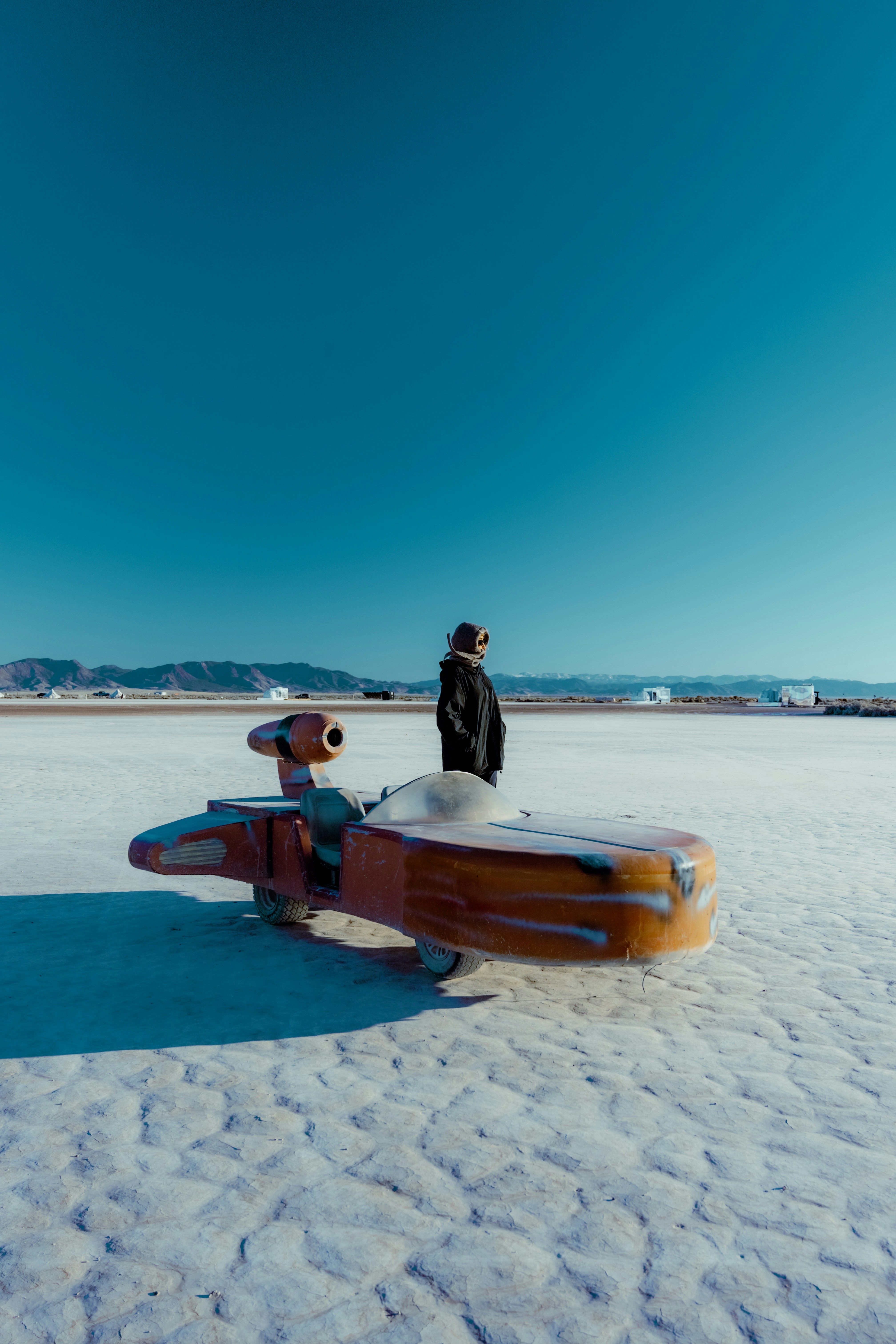 Person standing by a futuristic vehicle on a salt flat.