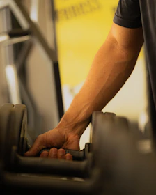 Man's hand reaching for a dumbbell in a gym.