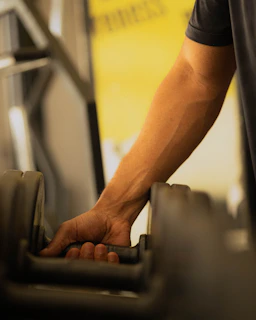 Man's hand reaching for a dumbbell in a gym.