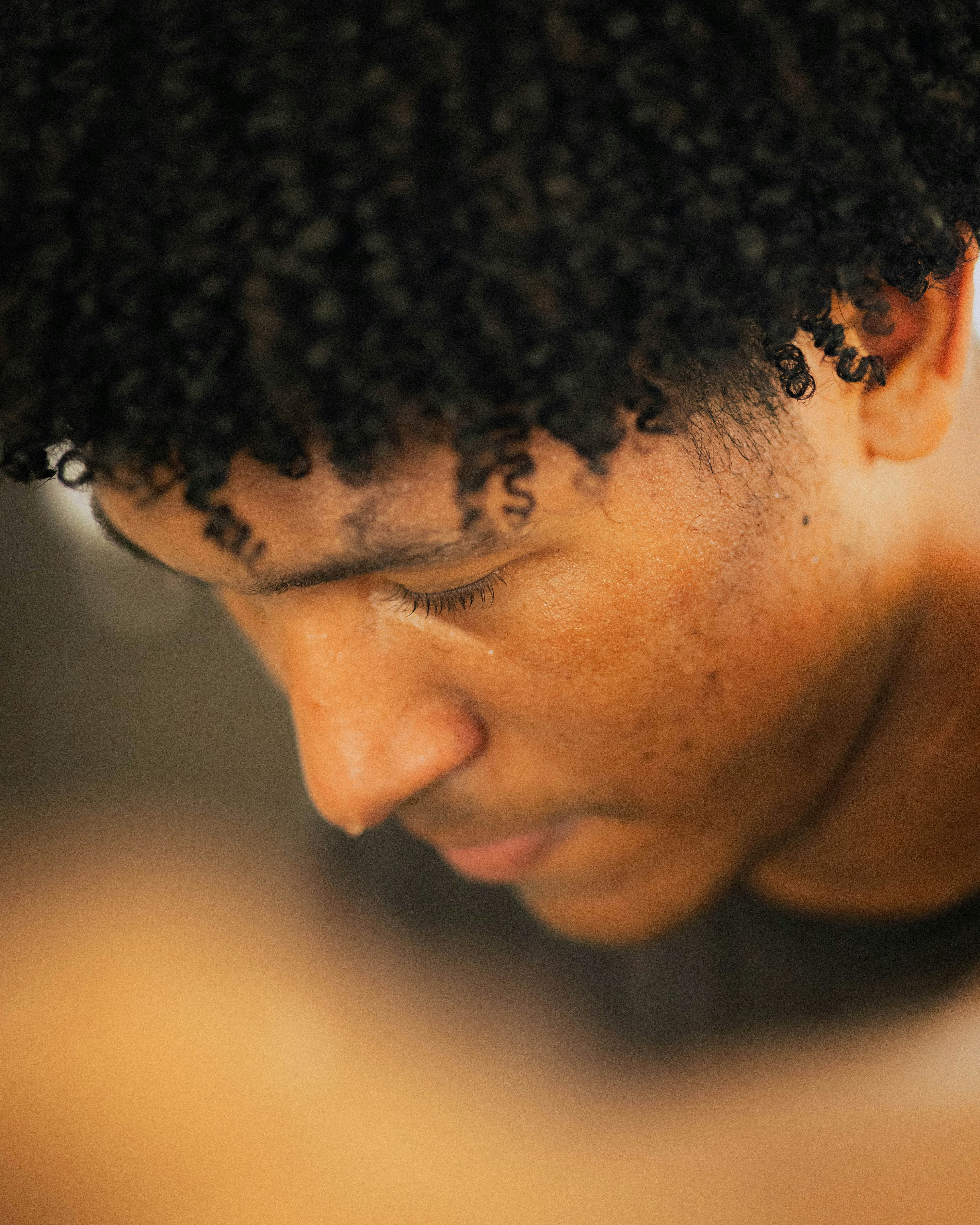 Close-up of a young man with curly hair looking down.