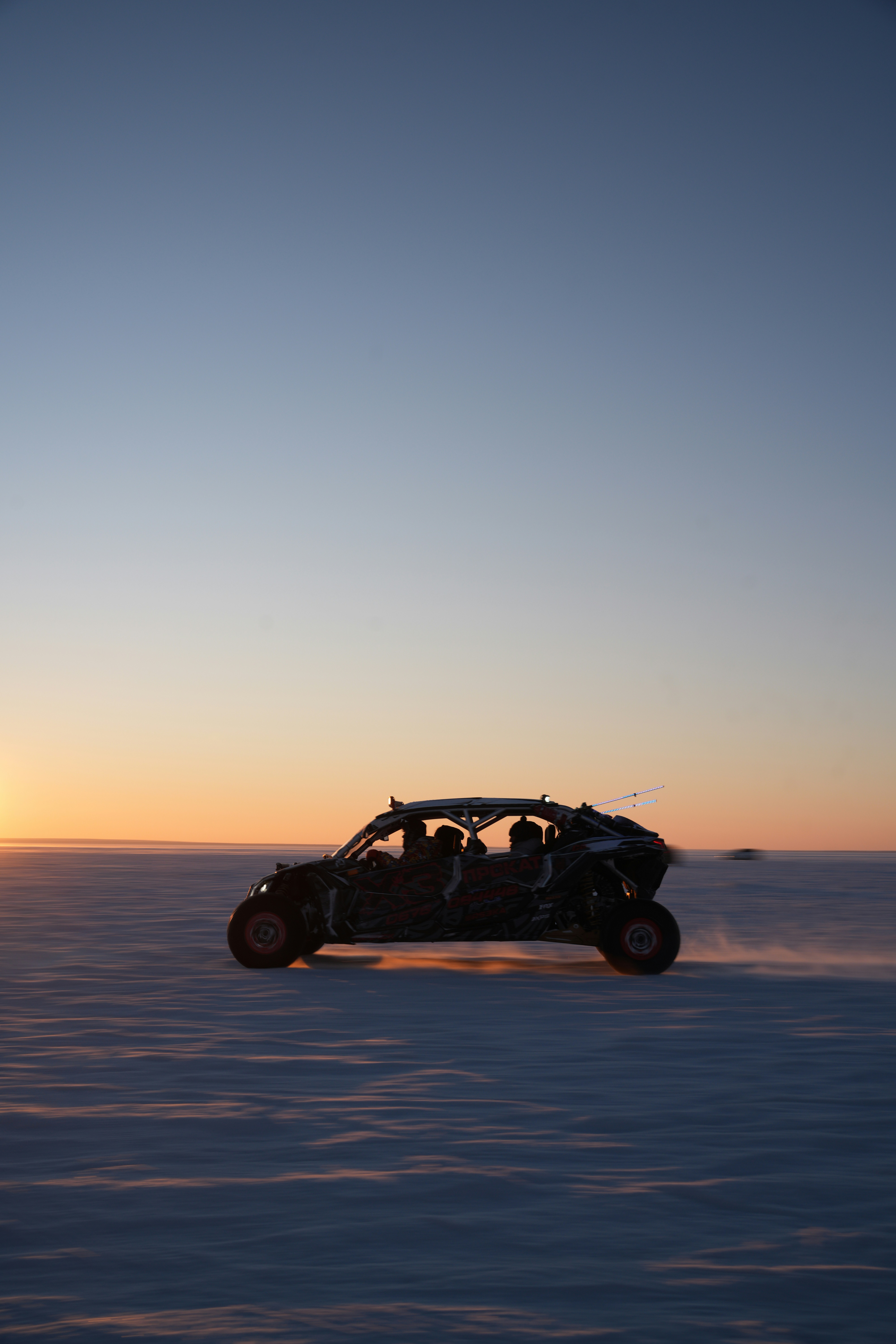 Off-road vehicle driving across a snowy landscape at sunset