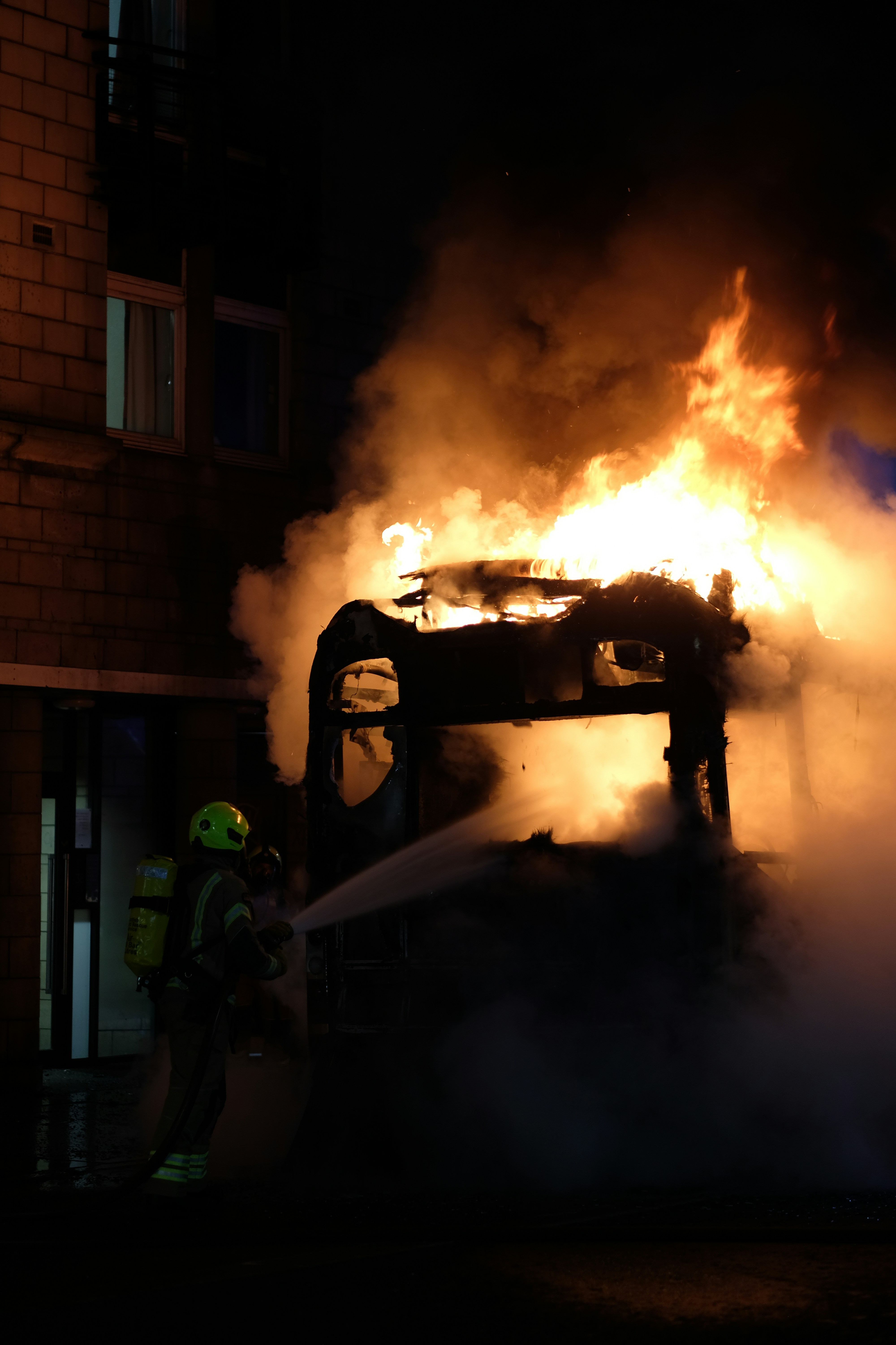 Firefighter sprays water on a burning vehicle at night