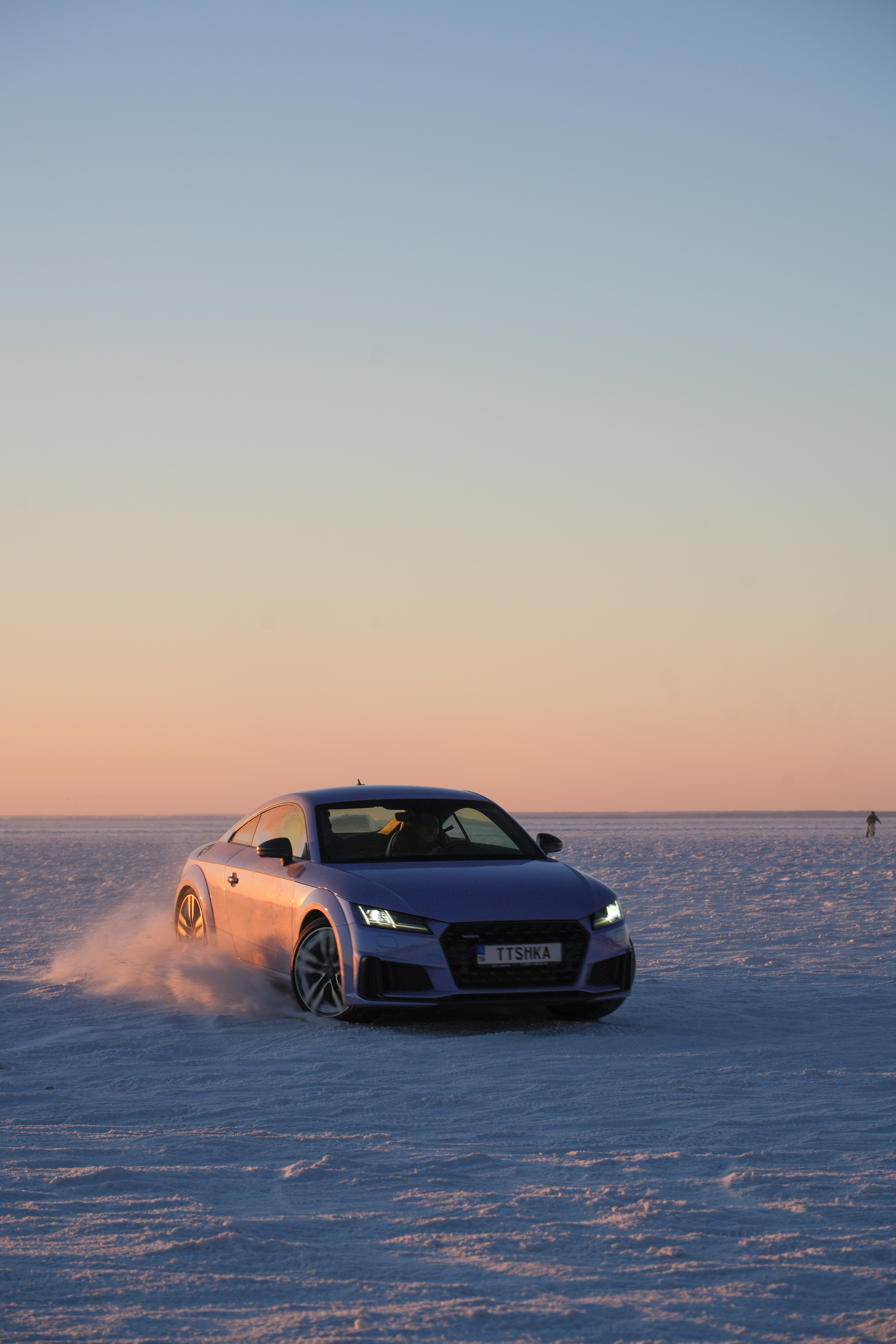 A purple car drifts on a vast, snow-covered plain.